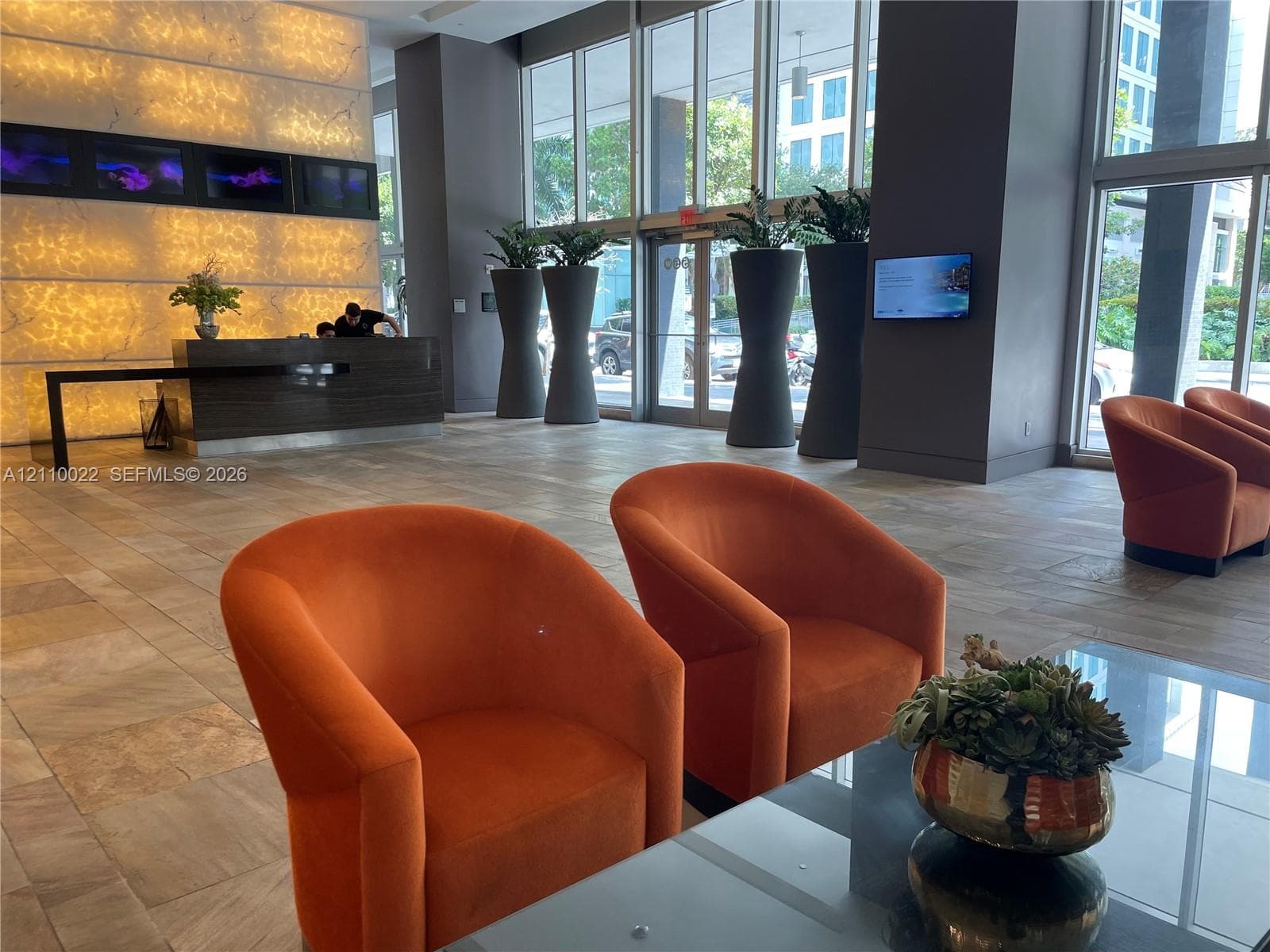 Lobby featuring full-height glass windows, backlit stone accent wall, stone-tile flooring, and built-in concierge desk