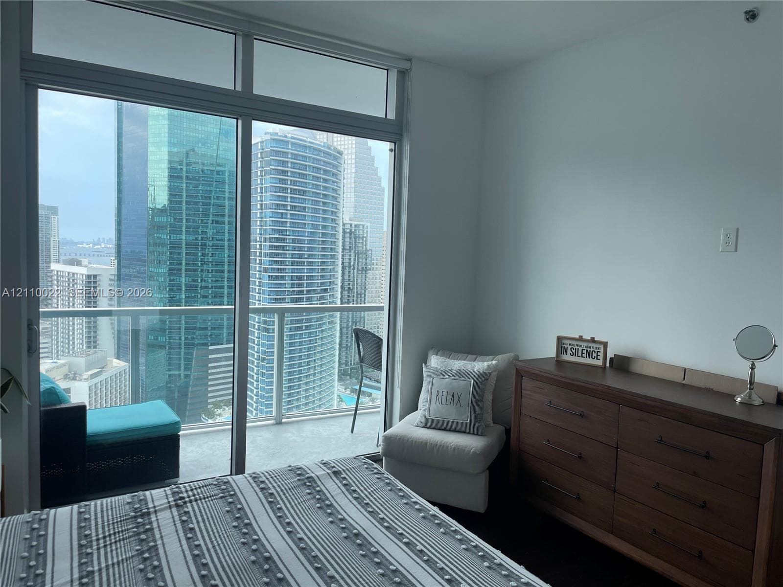Floor-to-ceiling glass sliding doors with an integrated transom window, opening to a private balcony with glass railing and urban skyline backdrop