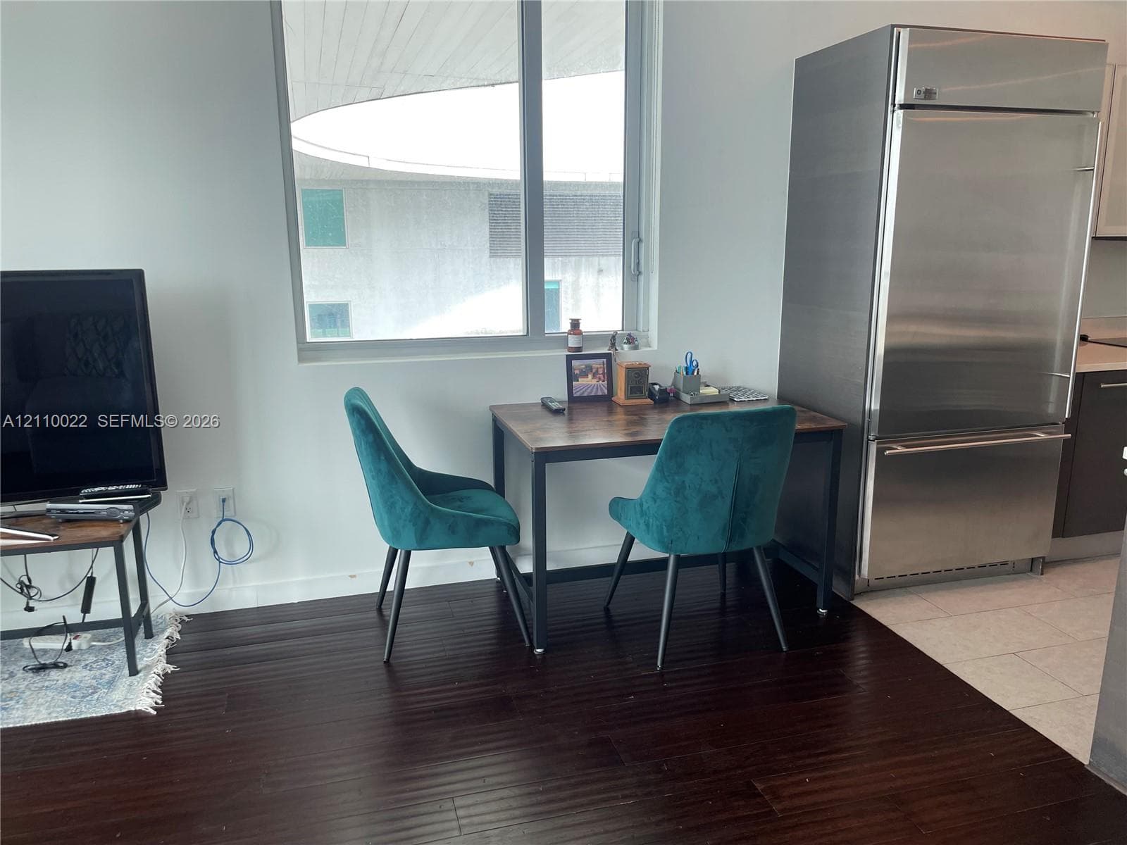 Stainless steel full-height refrigerator, dark-toned wood-finish flooring, and expansive window with sleek white wall finishes