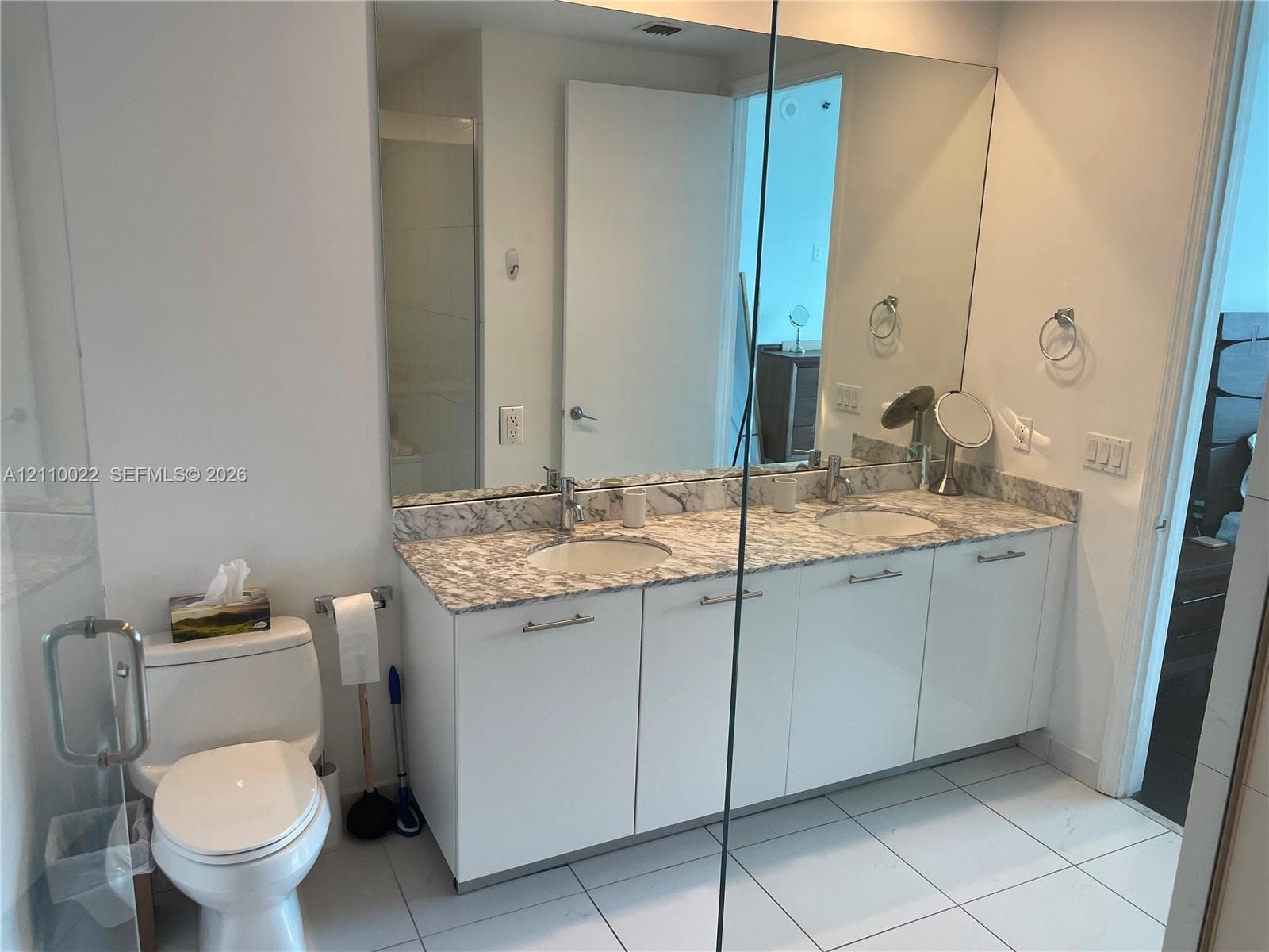 Dual-sink vanity with a solid-surface countertop, white gloss cabinetry, large wall-spanning mirror, and chrome fixtures
