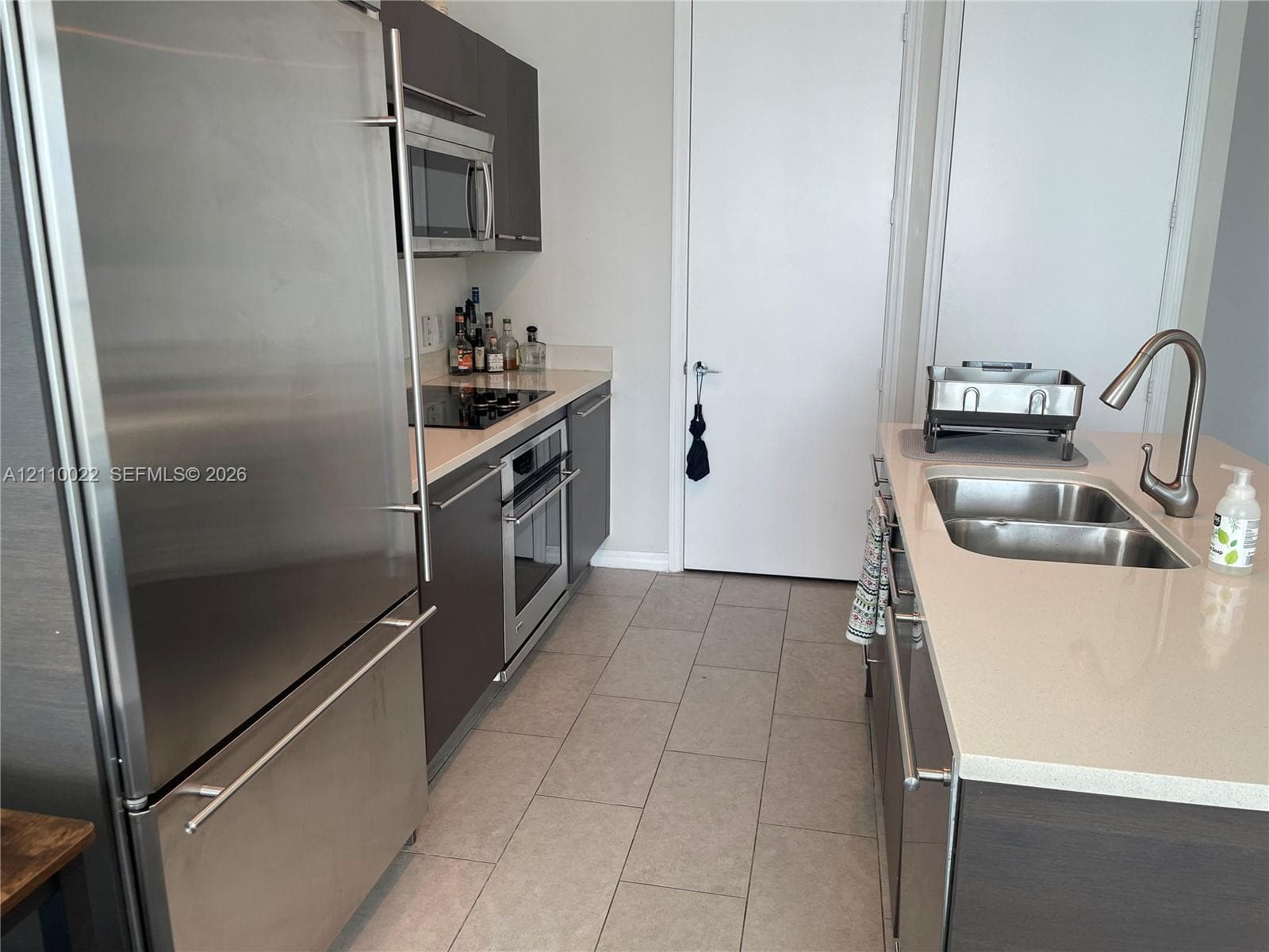 Kitchen featuring stainless steel appliances, flat-panel cabinetry, light-toned countertops, tile flooring, and a dual-basin sink with a gooseneck faucet