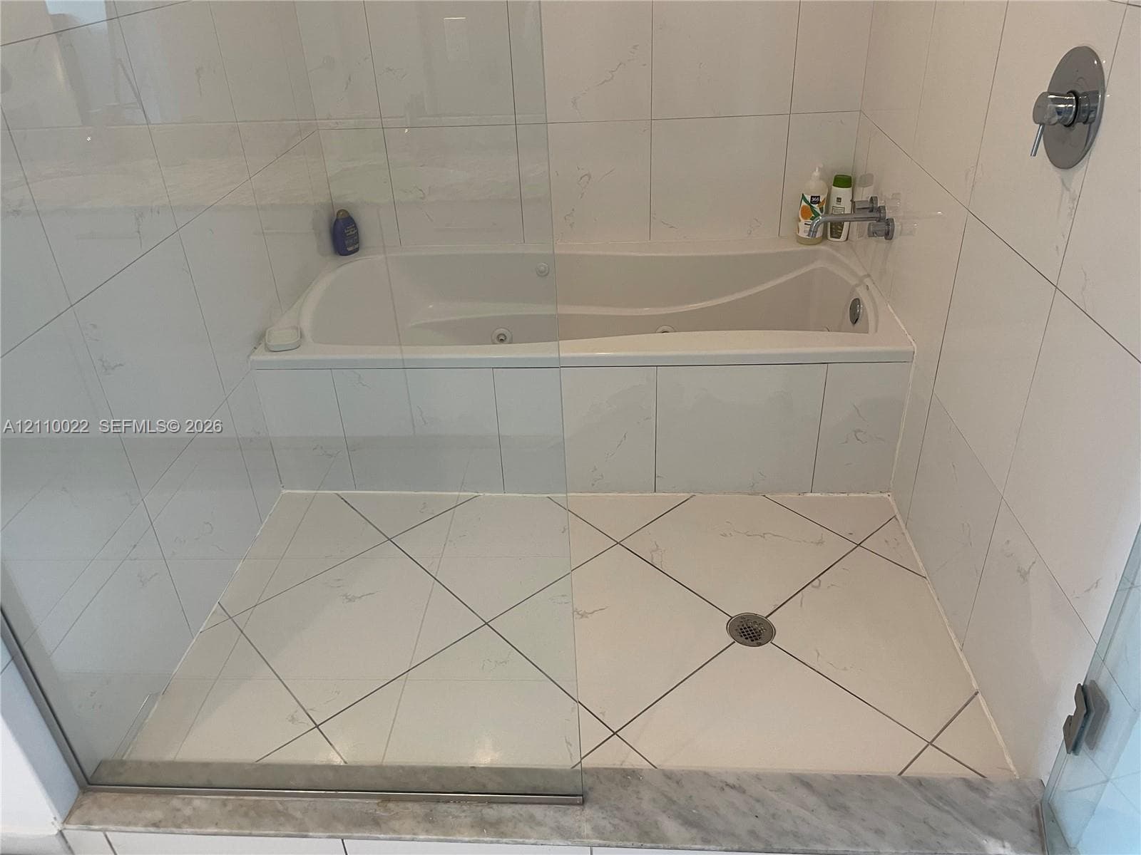 Walk-in shower enclosure with glass paneling, jetted soaking tub, white tile wall surround with veining, diagonal tile flooring, and polished chrome faucet fixtures