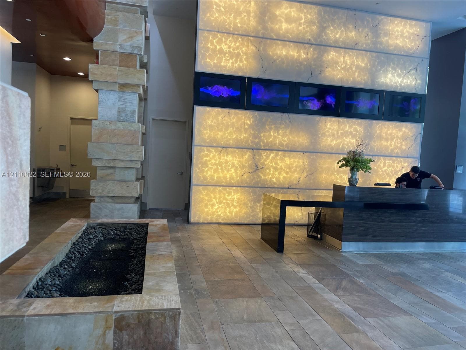Lobby featuring a backlit stone accent wall, stacked stone pillar, natural stone flooring, and a built-in stone-clad water feature