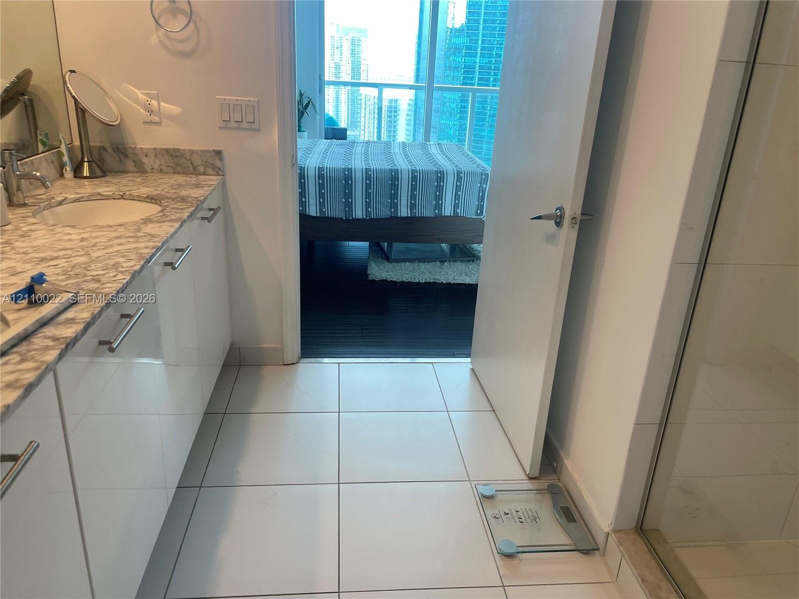 Bathroom featuring a stone-surface vanity with an integrated basin, glossy white cabinetry with silver-tone hardware, and large-format tile flooring, accompanied by a glass-enclosed shower