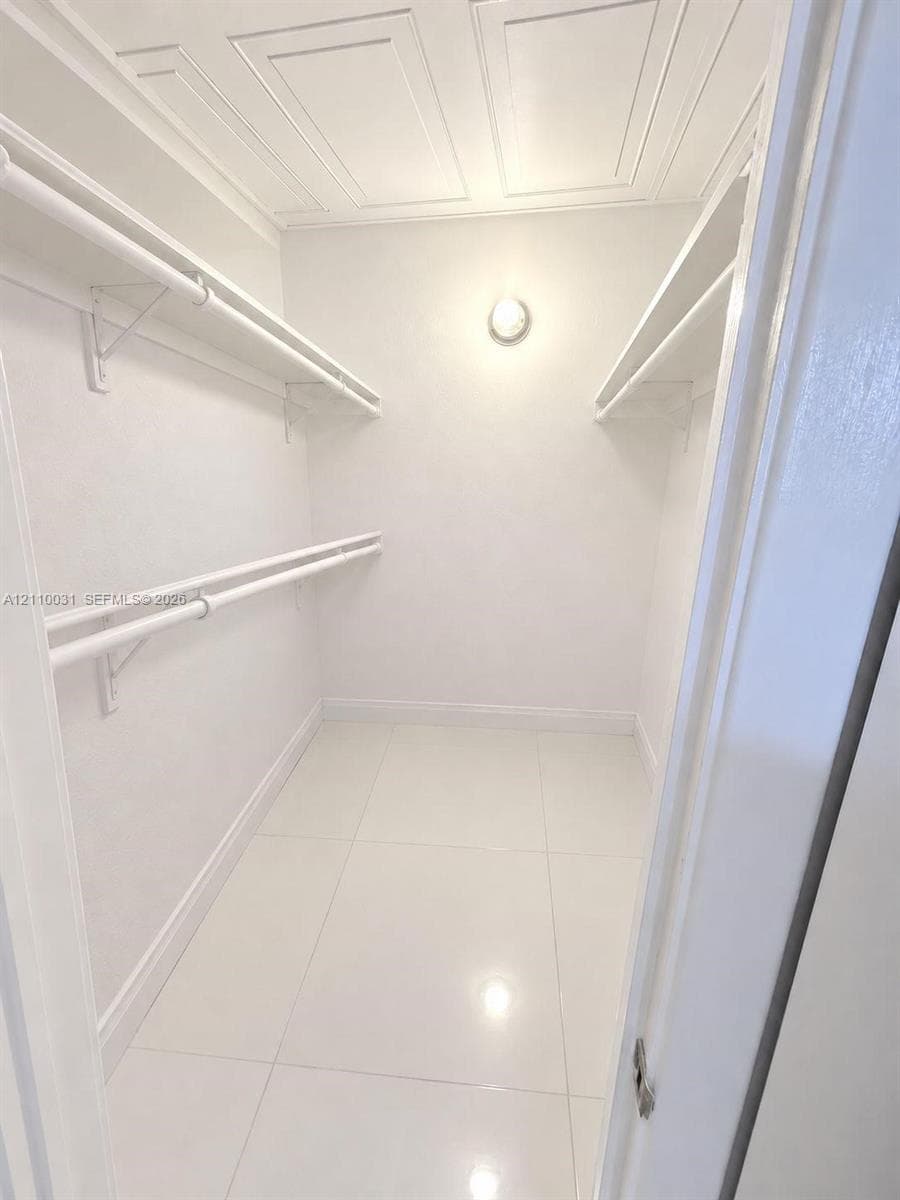 Walk-in closet featuring large-format tile flooring, multi-level wall-mounted shelving and hanging rods, ceiling molding, and a fixed circular wall-mounted light fixture