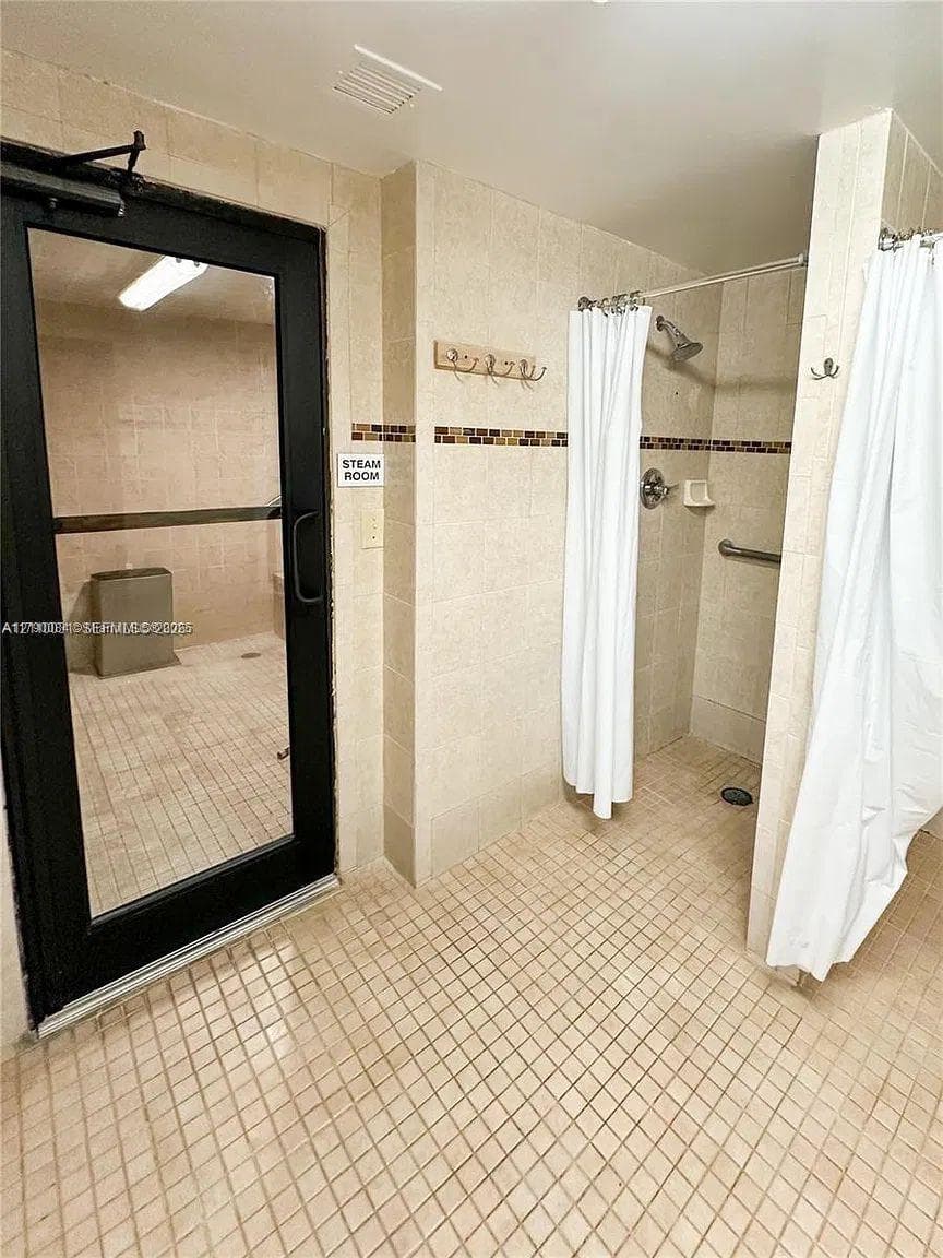 Steam room enclosed by a black-framed glass door, accompanied by a walk-in shower featuring wall-mounted hardware, tile surround, and mosaic accent tiling
