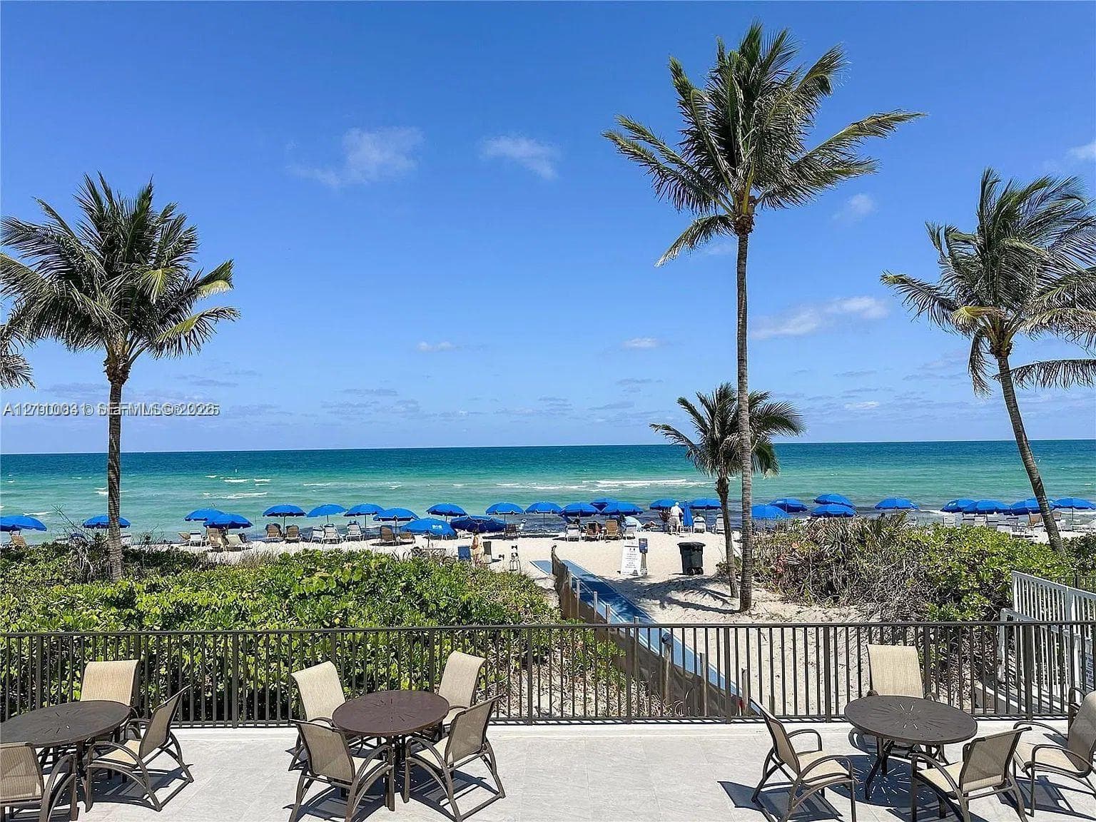 Stone-surfaced terrace featuring metal fencing, mature palm trees, and direct oceanfront positioning