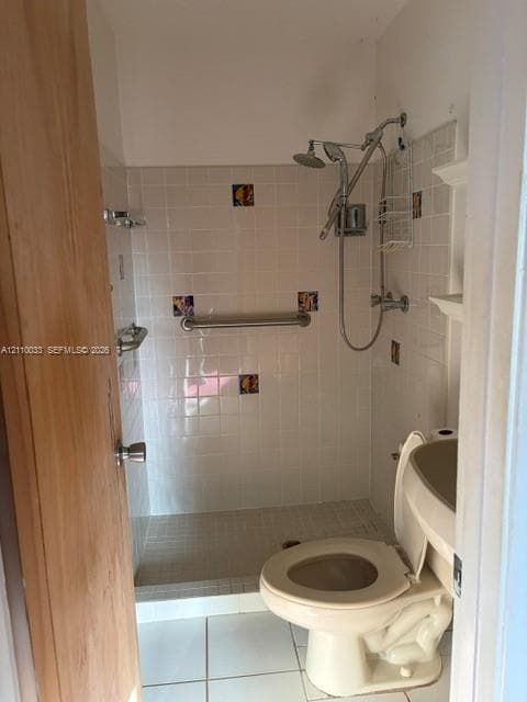 Walk-in shower enclosure featuring white ceramic wall tiles with decorative accent inlays, a built-in safety grab bar, a multi-setting shower head, and floor-level tile flooring