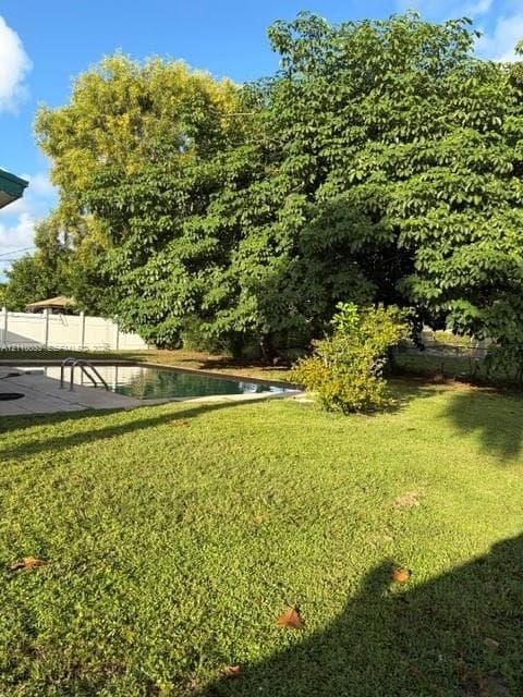 Backyard featuring an in-ground swimming pool, concrete pool deck, white vinyl perimeter fencing, and mature trees