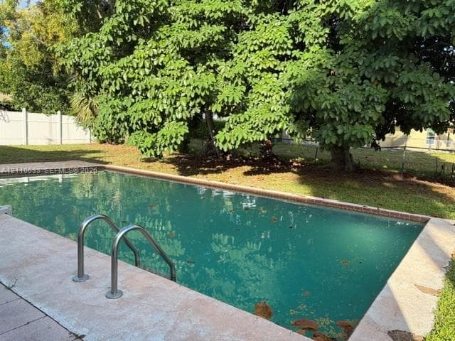 In-ground swimming pool with metal ladder, concrete decking, and perimeter fencing, surrounded by mature trees