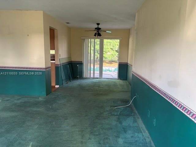 Carpeted flooring, dual-tone wall treatment with decorative border, ceiling-mounted fan with light fixture, and sliding glass doors