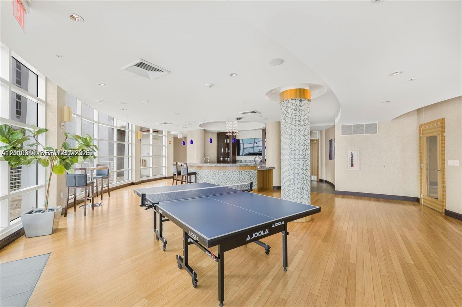 Recreational area featuring wood-finish flooring, floor-to-ceiling windows, a mosaic-tiled structural column, and a built-in wet bar with cabinetry