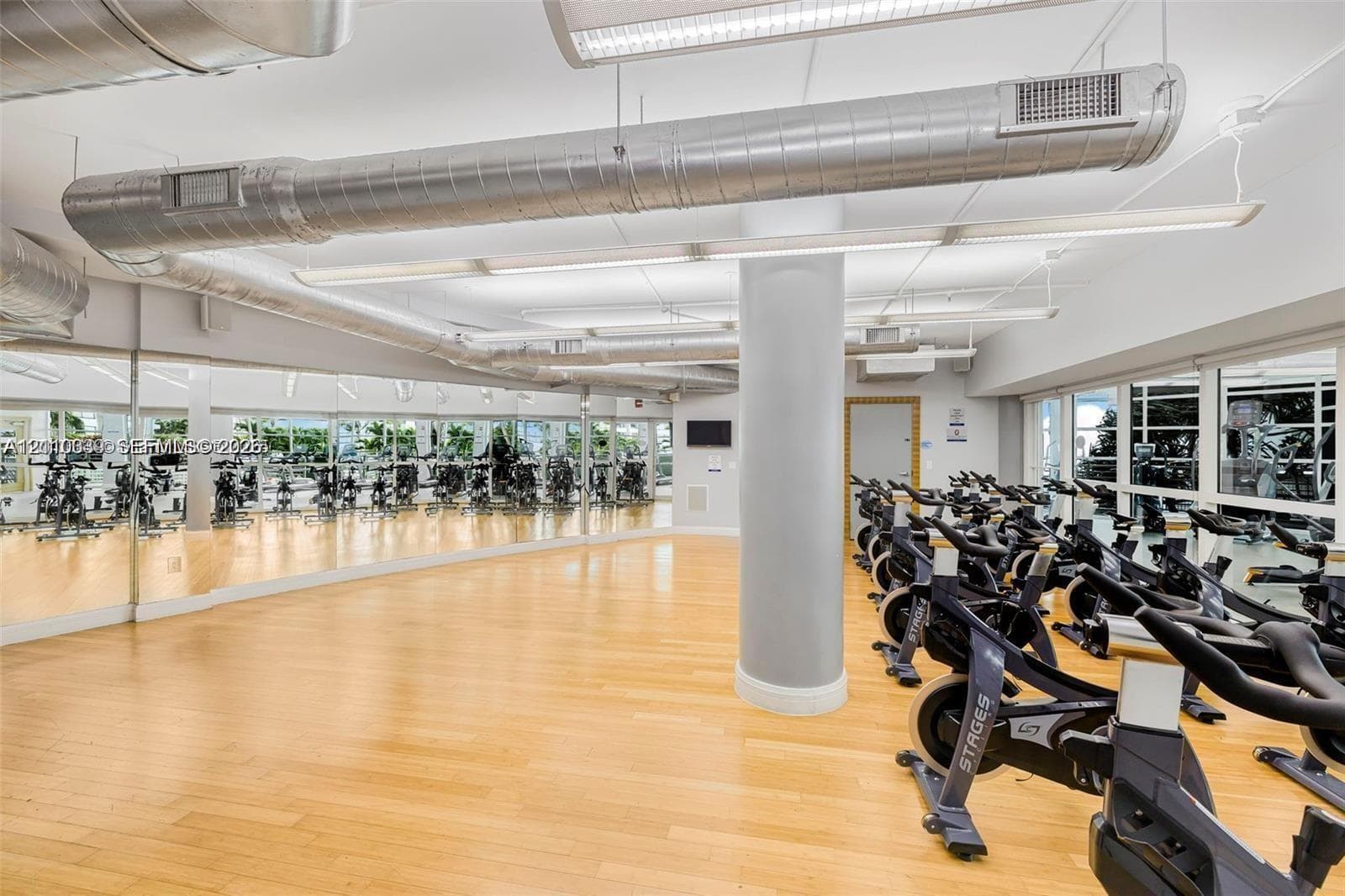 Industrial aesthetic featuring exposed metal ductwork, full-wall mirrors, light wood-finish flooring, and linear LED lighting
