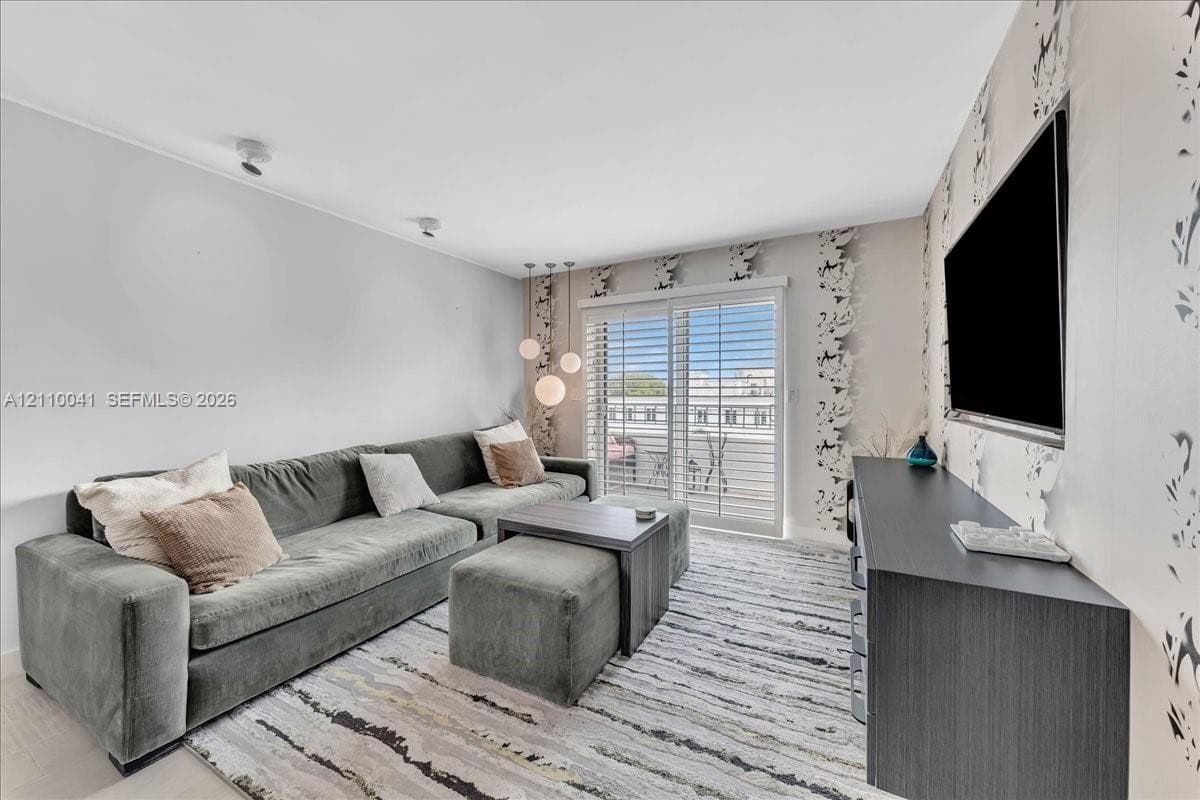 Living area featuring glass sliding doors with plantation shutters, recessed ceiling lighting, three-globe pendant lighting, and an accent wall with patterned wall covering