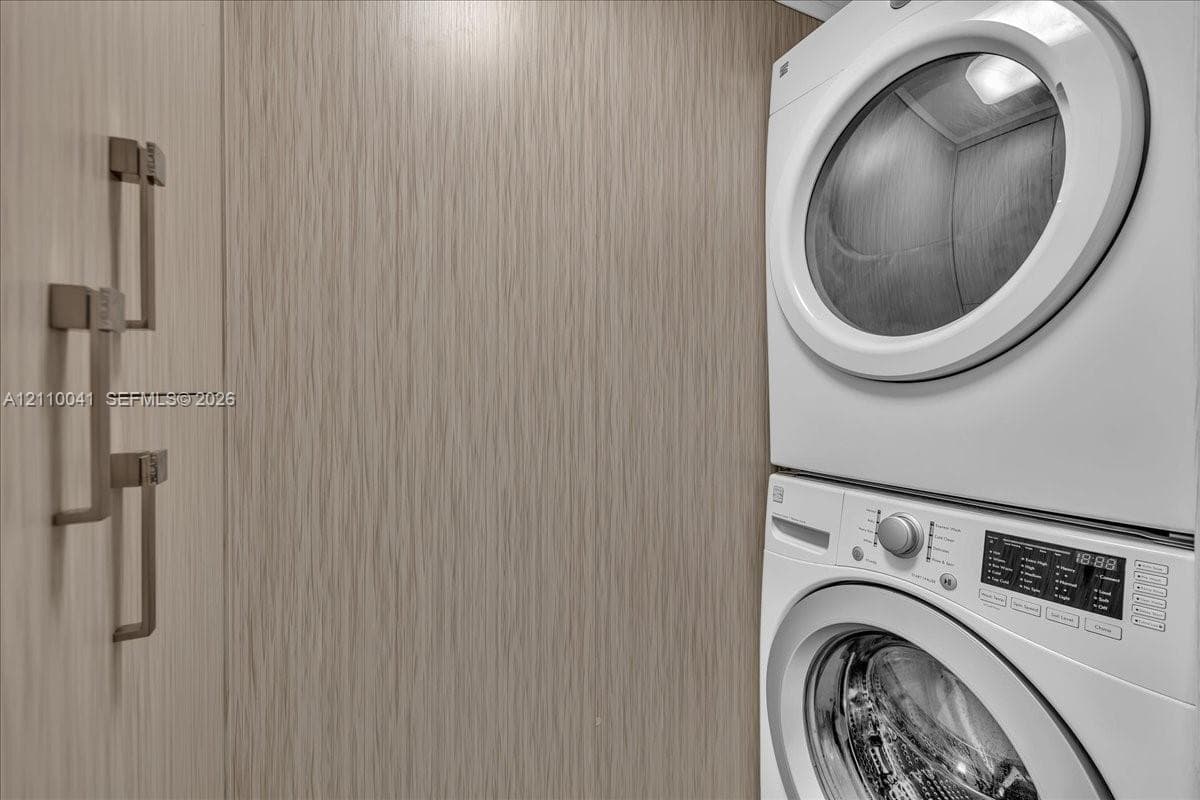 Stacked washer and dryer unit featuring built-in cabinetry with metallic bar hardware and a light-toned wood-finish exterior