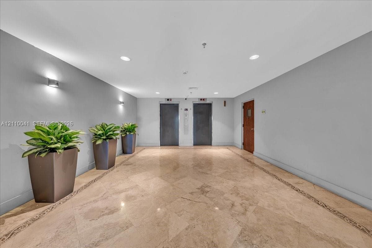 Common area lobby featuring polished stone flooring with decorative inlay, dual elevator banks, and recessed ceiling lighting