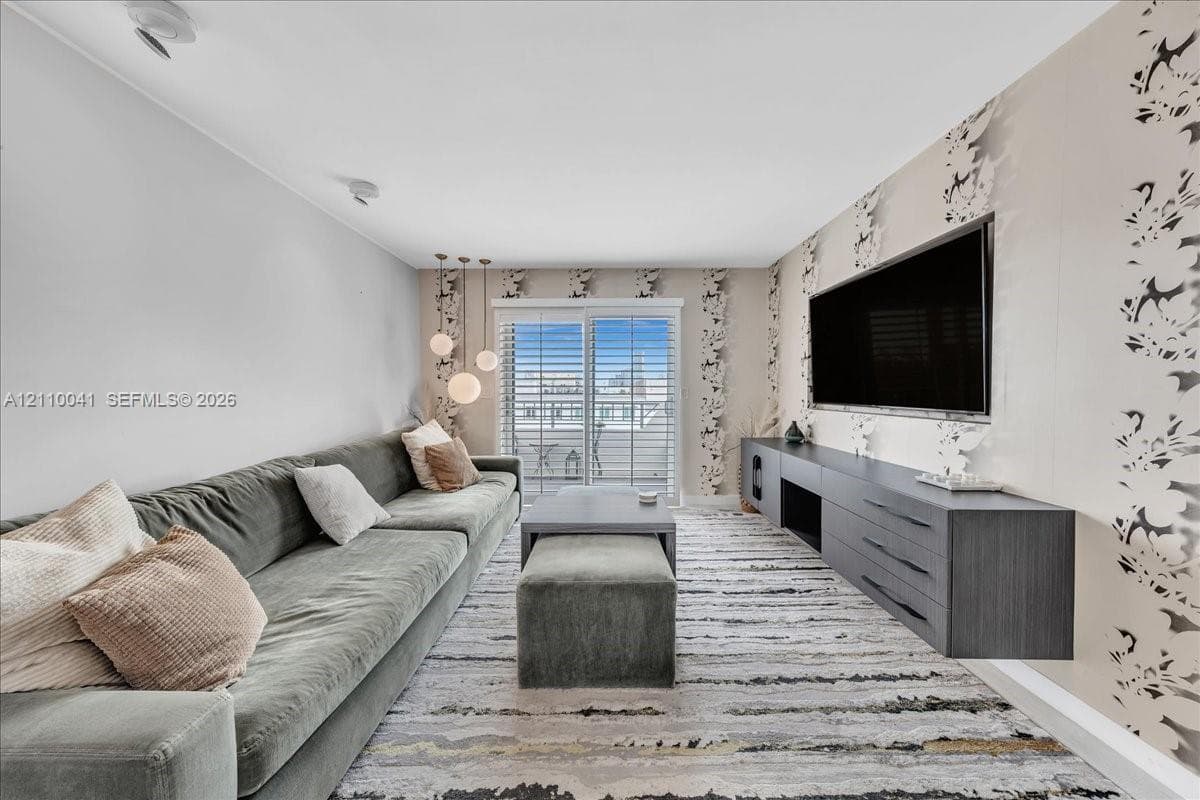 Floating charcoal-finish media console, patterned accent wallpaper, glass sliding doors with plantation shutters, and a trio of pendant lights