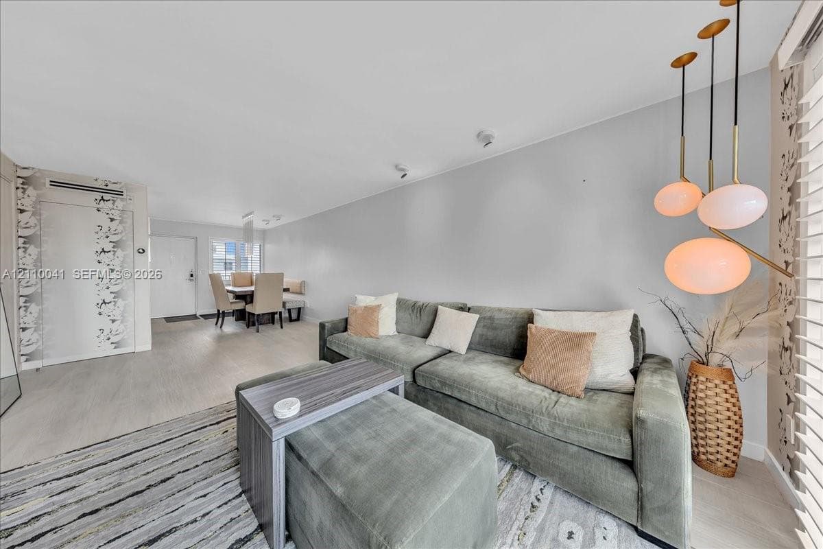 Multi-pendant brass light fixture, wood-finish flooring, patterned wallpaper accent wall, and horizontal window blinds