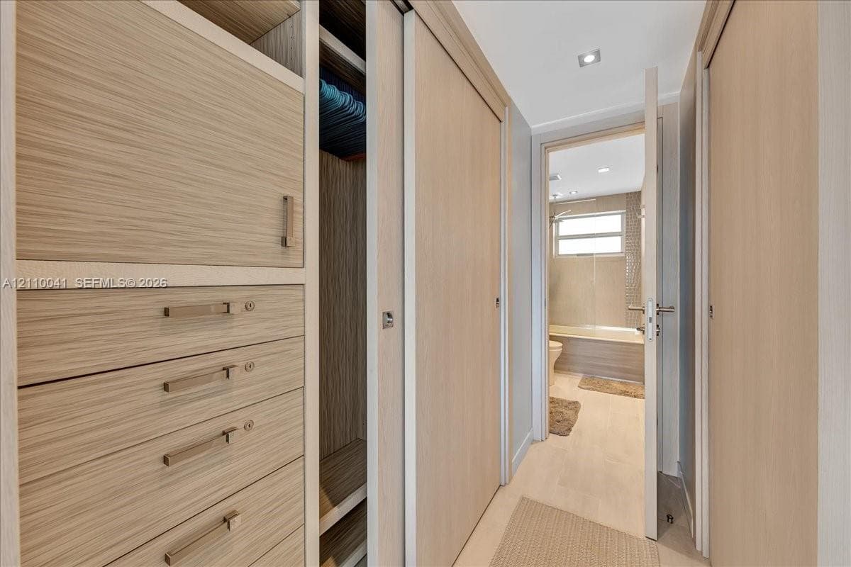 Built-in wood-finish cabinetry featuring integrated drawers, sliding closet doors, recessed ceiling lighting, and polished metal hardware