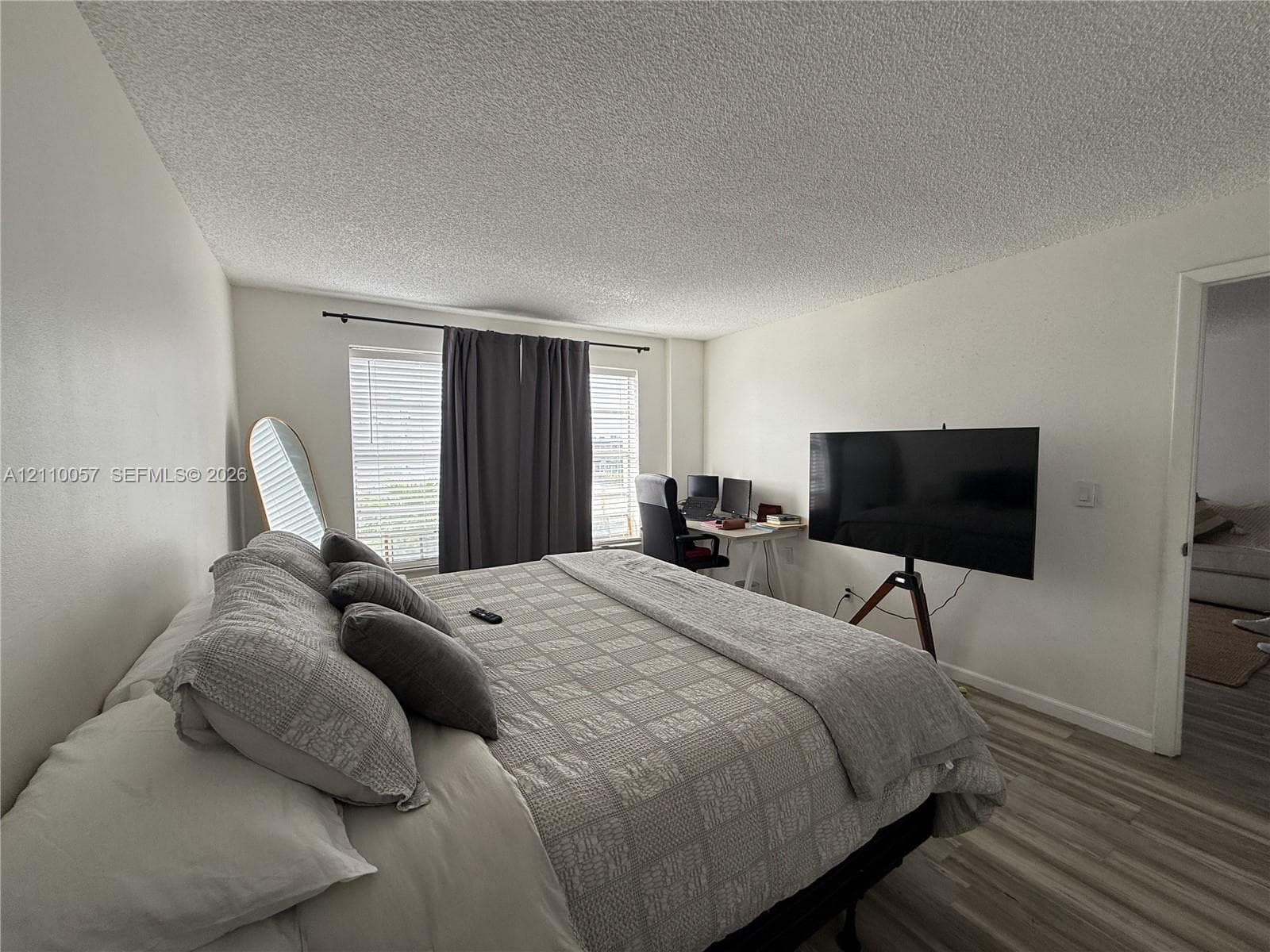Room featuring textured ceiling, dual windows with black curtain hardware, and wood-finish flooring