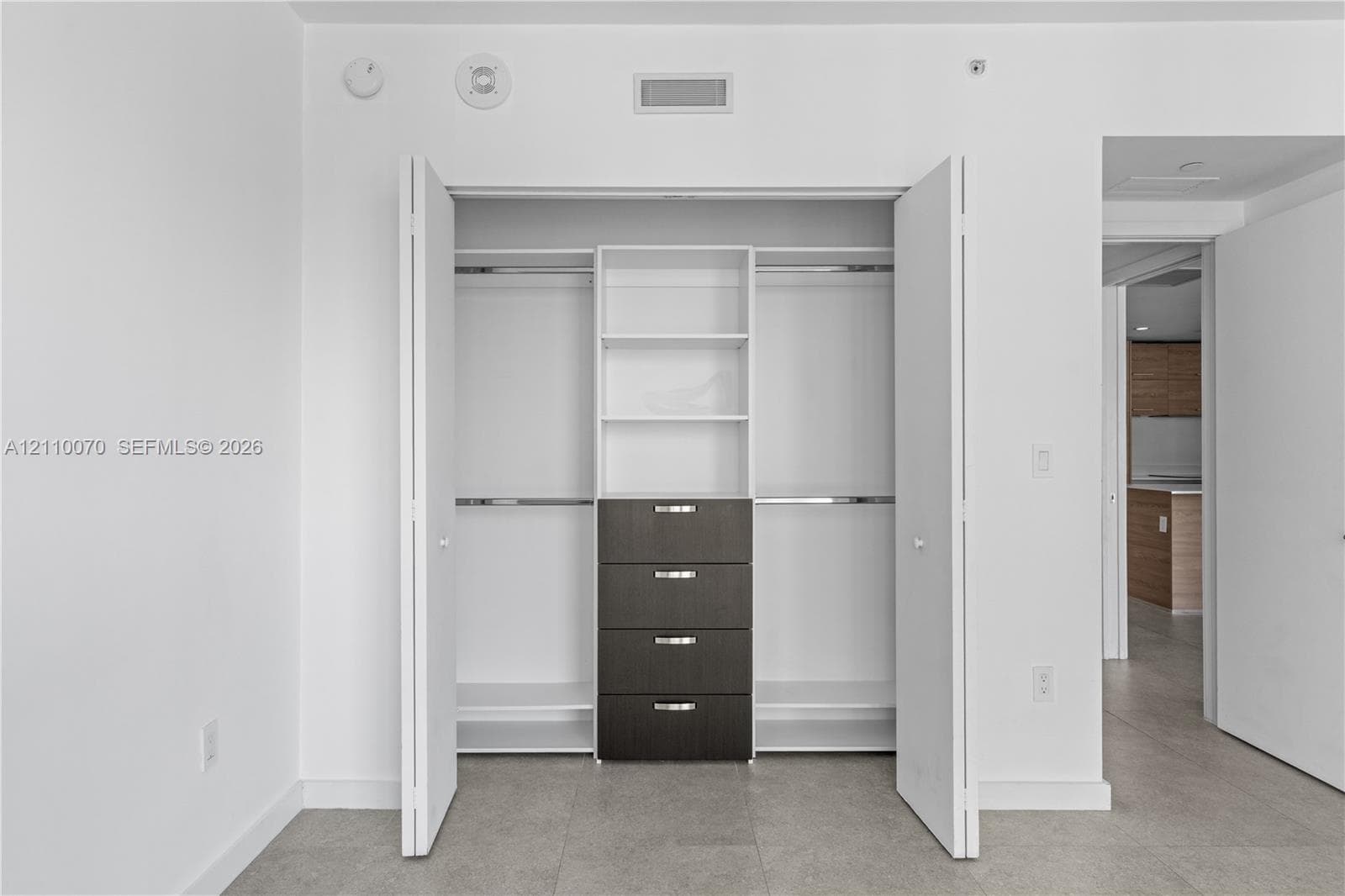 Closet featuring white bi-fold doors, integrated shelving, and a dark-finish four-drawer dresser unit