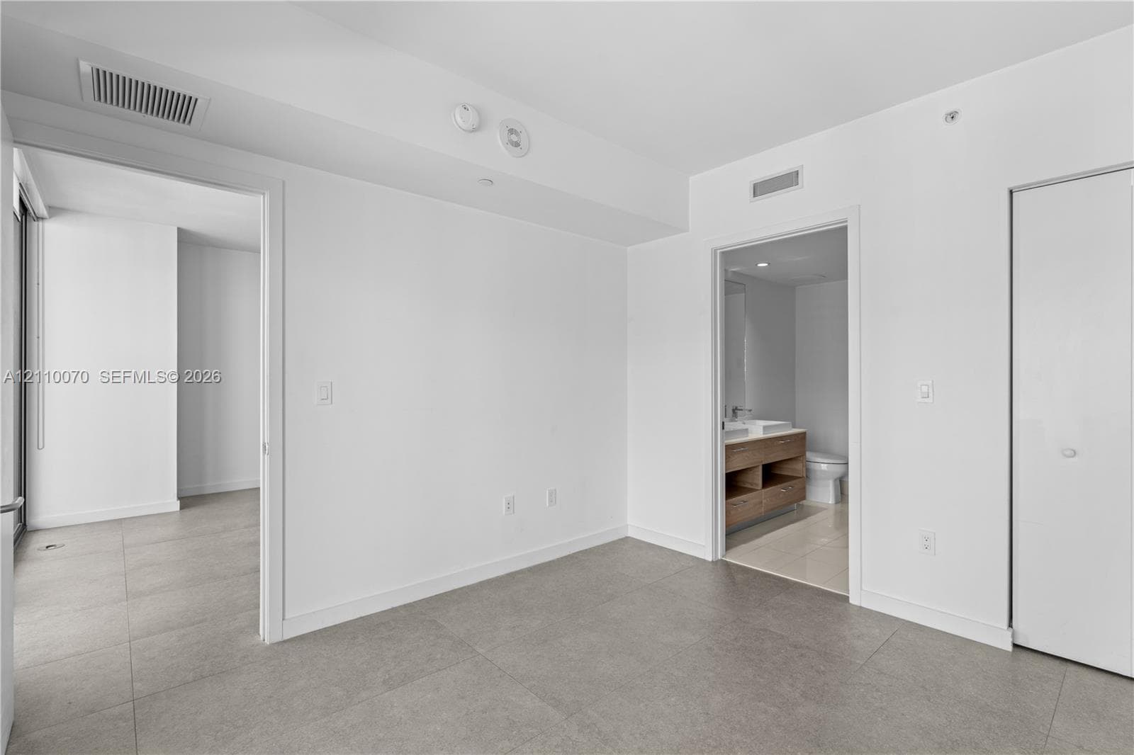 Large-format neutral floor tiling, clean white wall finishes, and a reach-in closet with sliding doors