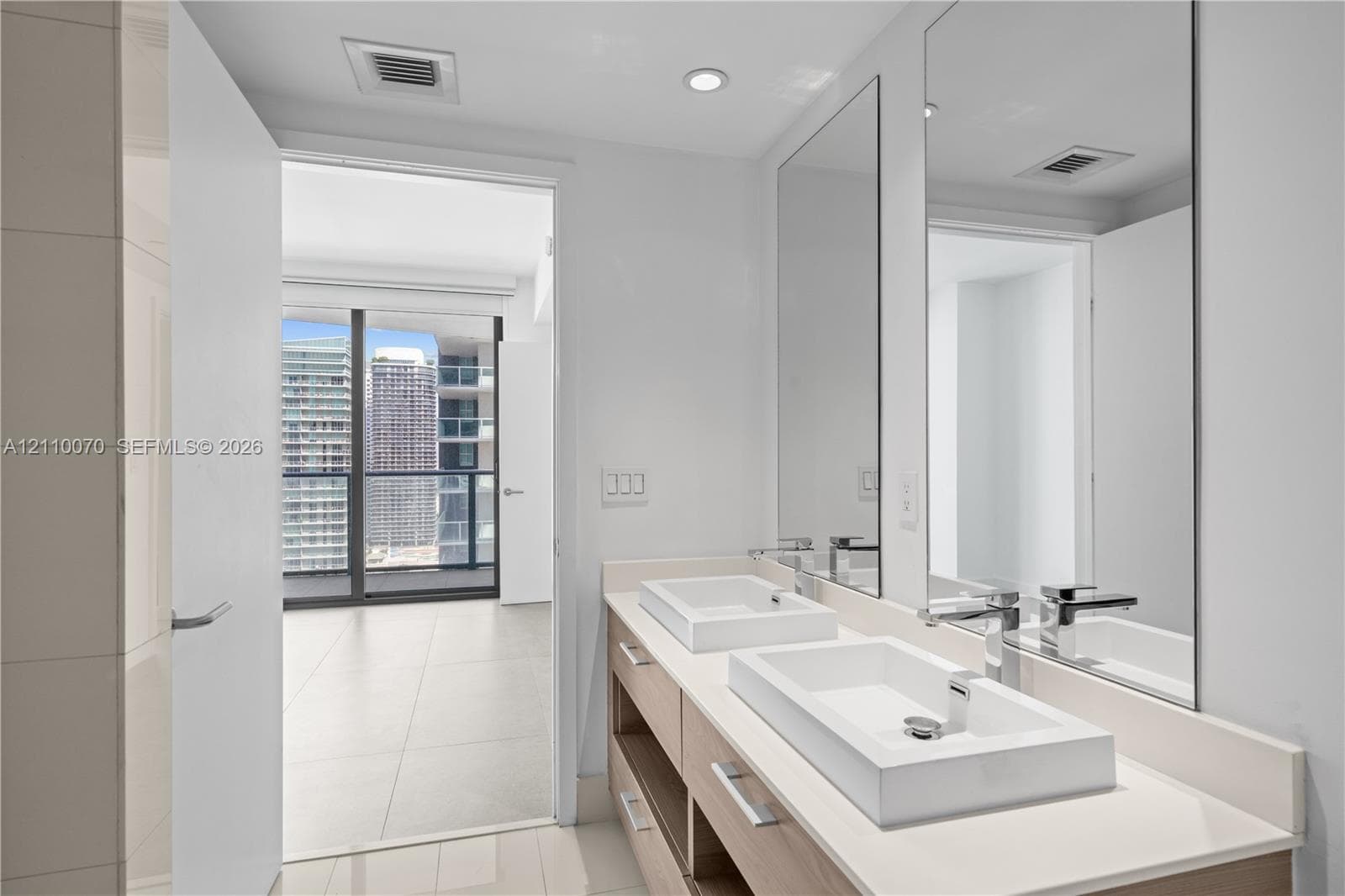 Bathroom featuring a dual-sink vanity with rectangular vessel sinks, light wood-tone cabinetry, quartz countertops, and floor-to-ceiling vanity mirrors