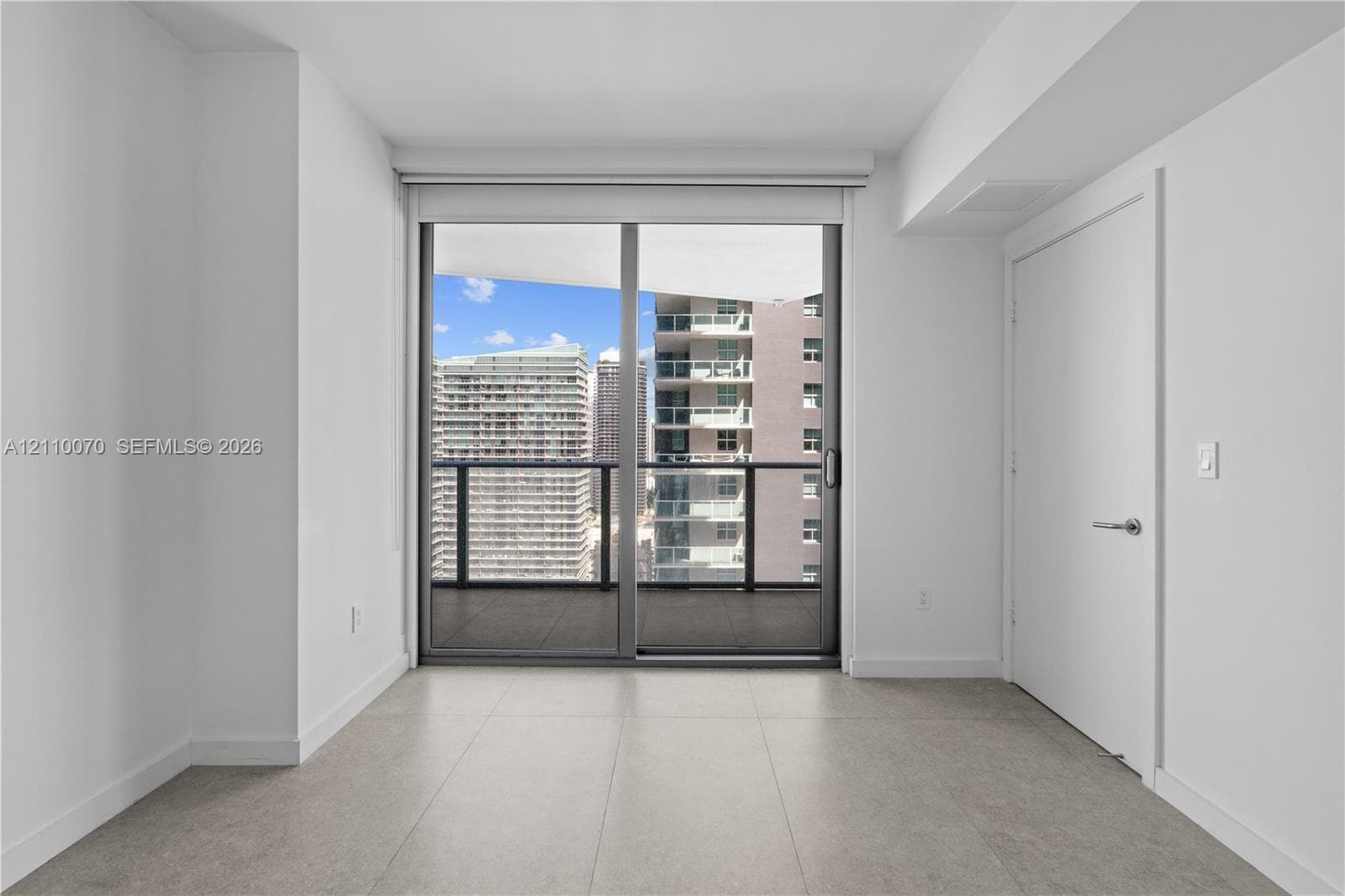 Large-format ceramic floor tiling, full-height glass sliding door, private balcony with metal railing, and neutral wall finishes