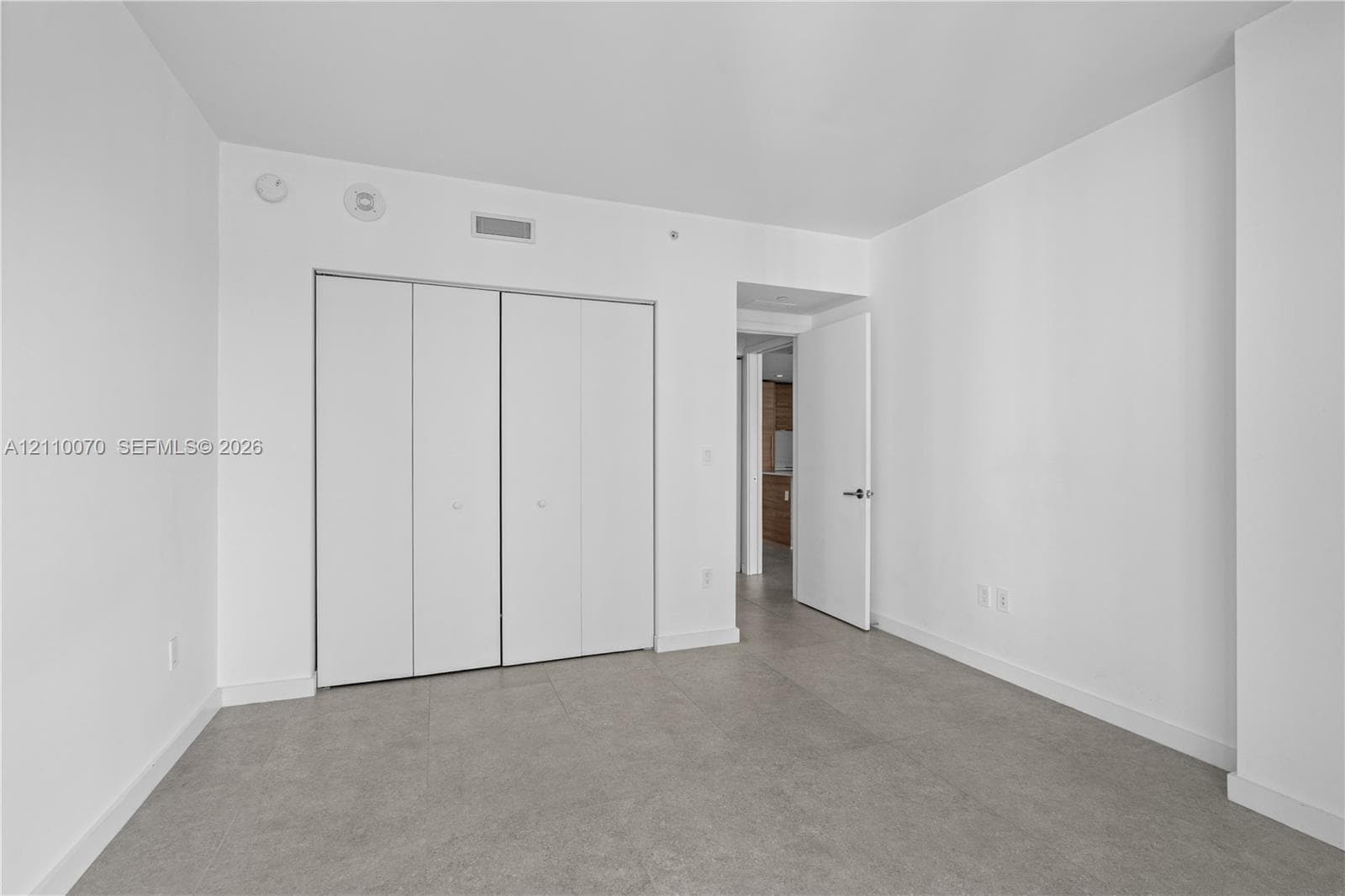 Neutral interior featuring large-format tile flooring, crisp white walls, and a multi-panel floor-to-ceiling closet