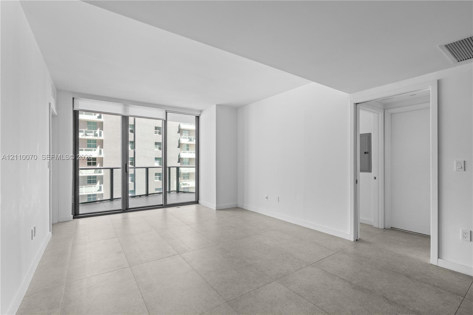 Floor-to-ceiling glass sliding doors, private balcony, neutral large-format tile flooring, and crisp white wall finishes