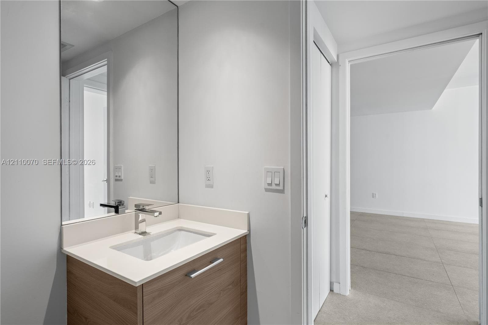 Bathroom vanity featuring a wood-finish cabinet, rectangular basin, neutral solid-surface countertop, and full-height wall mirror