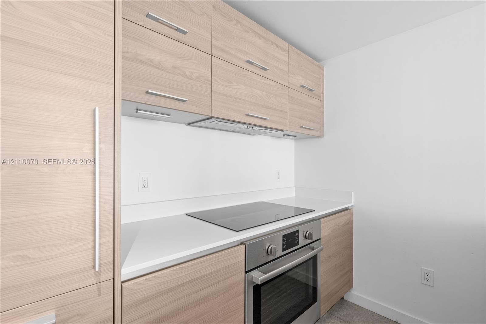 Flat-panel wood-finish cabinetry, solid-surface countertops, built-in stainless steel oven, and integrated cooktop