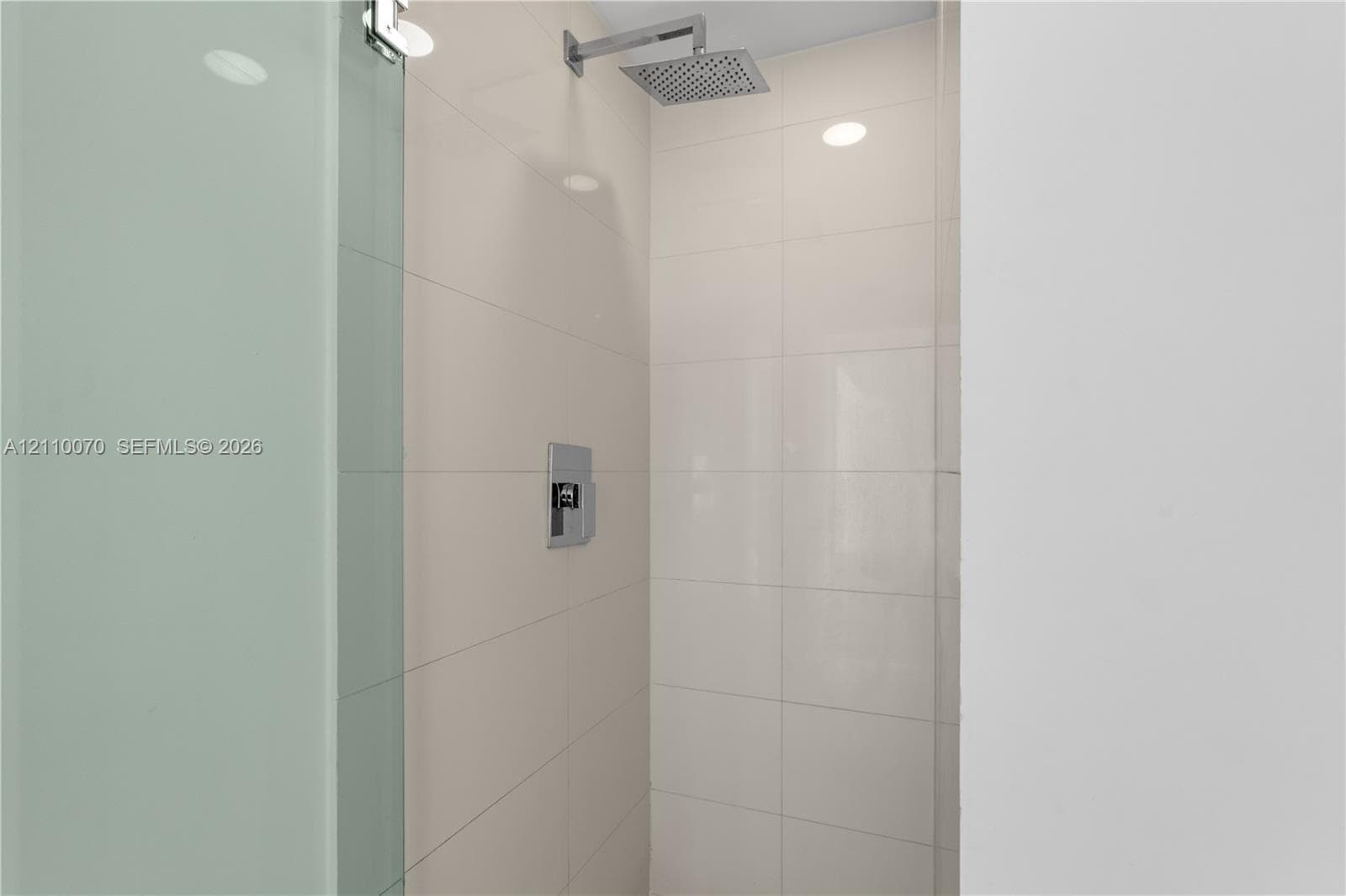 Walk-in shower featuring large-format ceramic tile, glass enclosure, and a chrome overhead rainfall showerhead