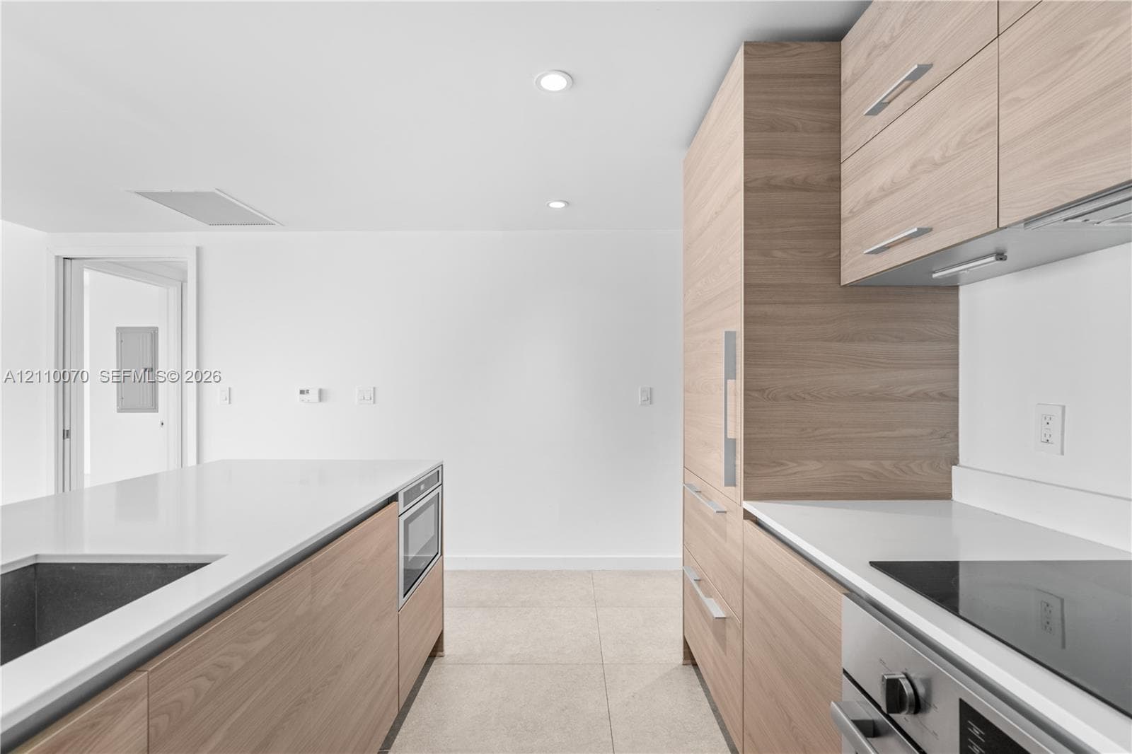 Kitchen featuring wood-finish cabinetry, white solid-surface countertops, integrated stainless steel appliances, recessed lighting, and large-format tile flooring