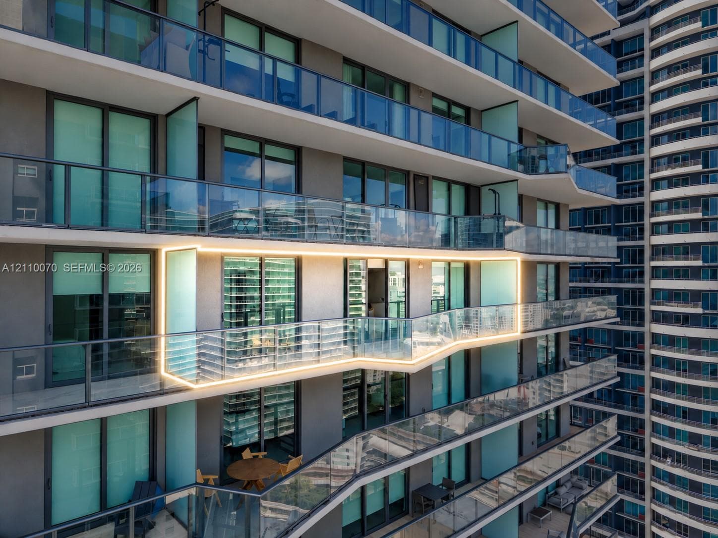 High-rise exterior featuring stepped balconies, floor-to-ceiling glass paneling, integrated glass railing systems, and concrete structural elements