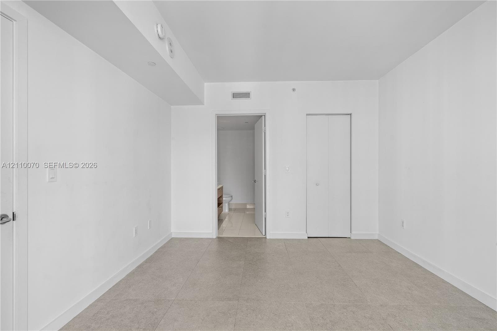 Neutral-toned room featuring large-format tile flooring, smooth ceiling finishes, and a double-door closet