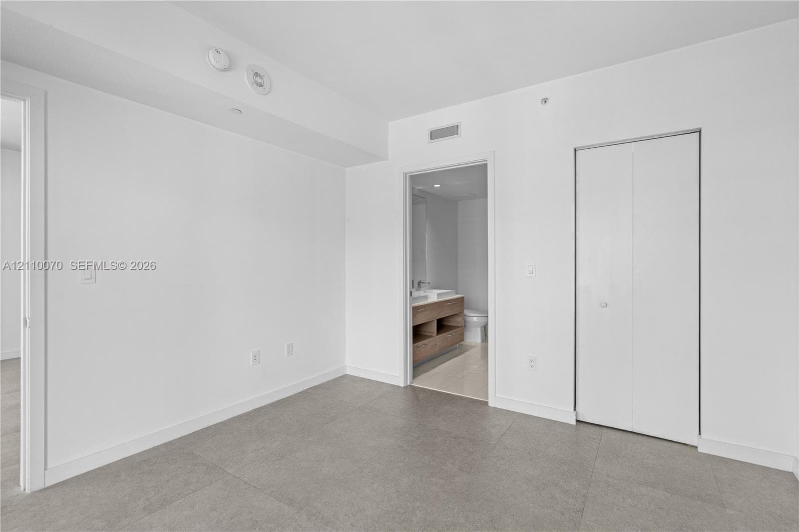 Neutral-toned floor tiling, bi-fold closet doors, and smooth, high-contrast wall finishes