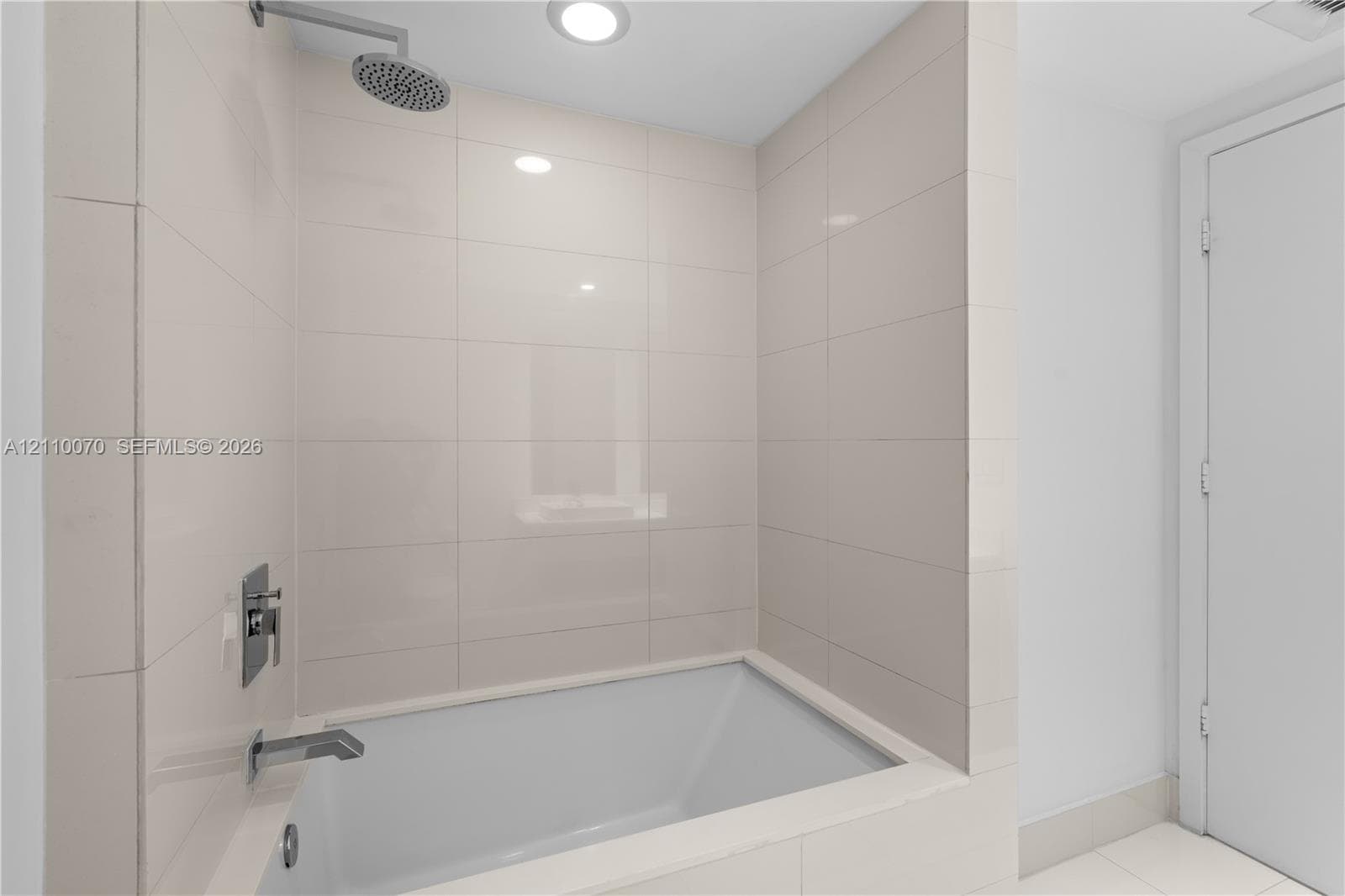 Deep-soaking bathtub with rectangular integrated surround, wall-mounted chrome rainfall showerhead, and polished chrome hardware