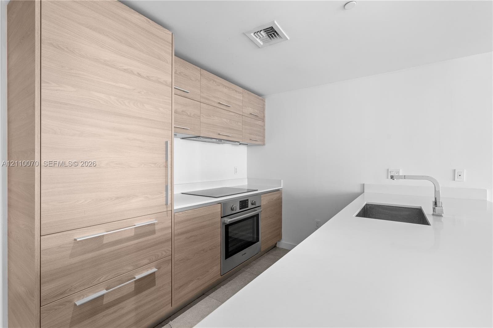 Modern kitchen featuring flat-panel wood-finish cabinetry, white solid-surface countertops, built-in stainless steel appliances, and an undermount sink with a gooseneck faucet