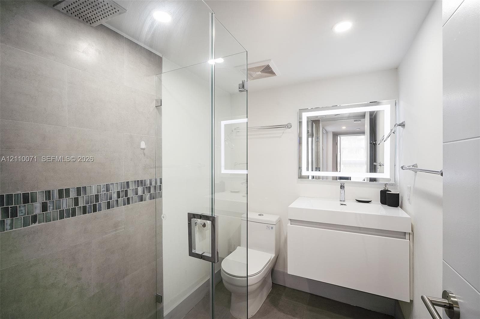 Walk-in shower with a rain-style showerhead, glass enclosure, and decorative tile inlay, featuring a floating vanity with an integrated sink and an LED-backlit mirror