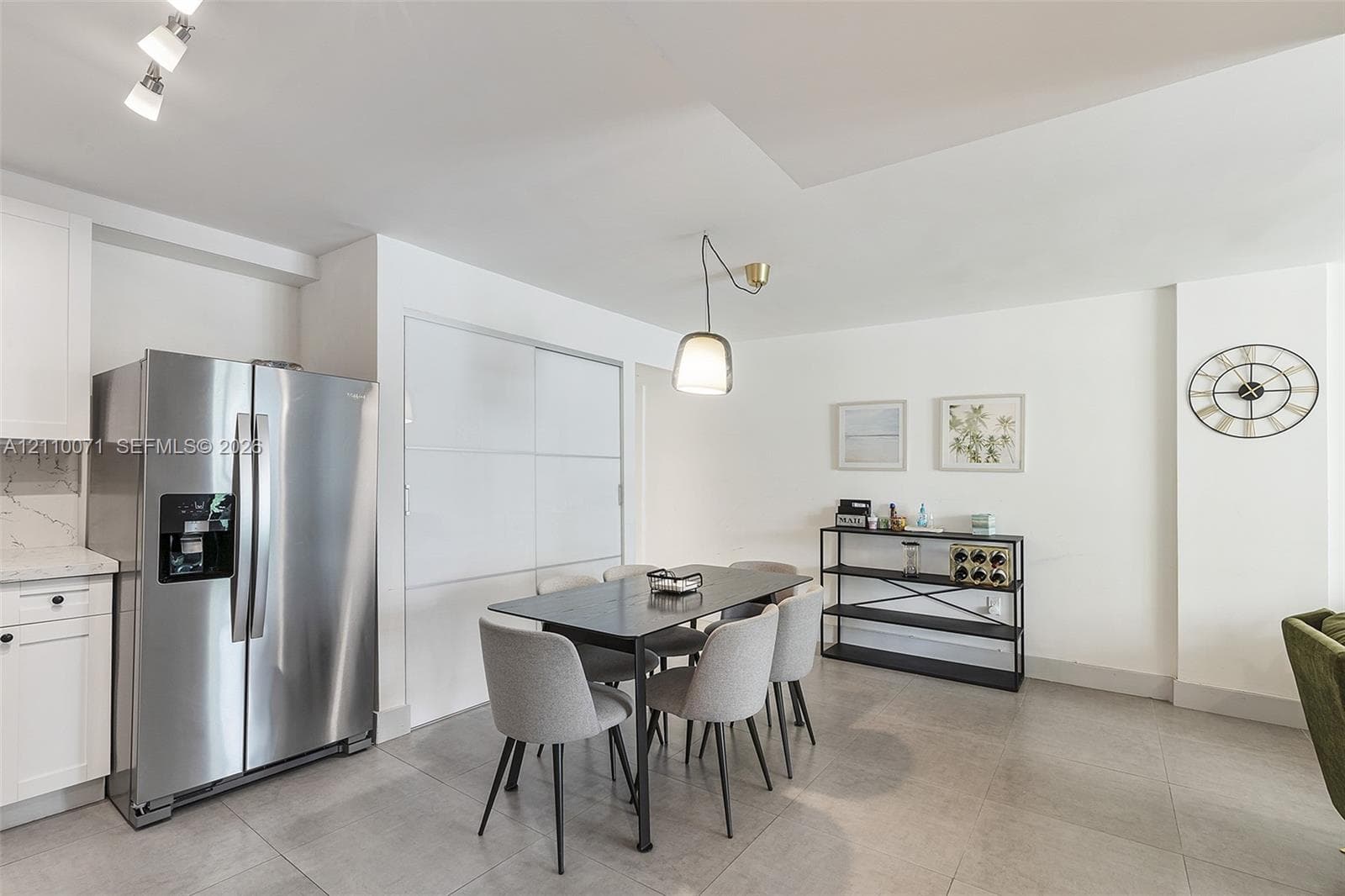 Stainless steel side-by-side refrigerator, white shaker-style cabinetry, matte tile flooring, contemporary pendant lighting, and built-in closet with sliding panels