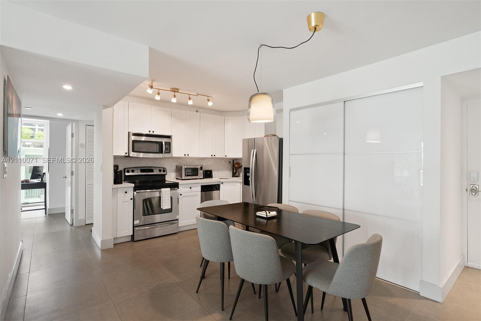 Kitchen area featuring white shaker-style cabinetry, stainless steel appliances, solid-surface countertops, tile flooring, and modern overhead pendant lighting