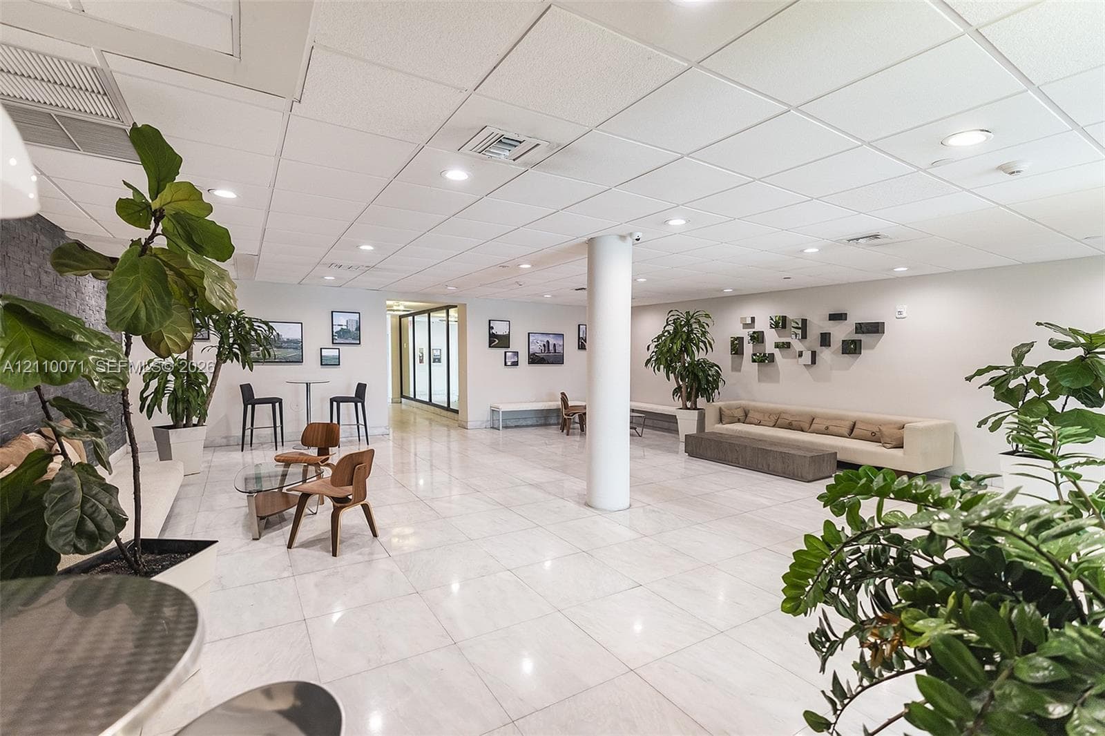 Spacious lobby featuring polished stone flooring, recessed ceiling lighting, grid-pattern drop ceiling, and a central structural column