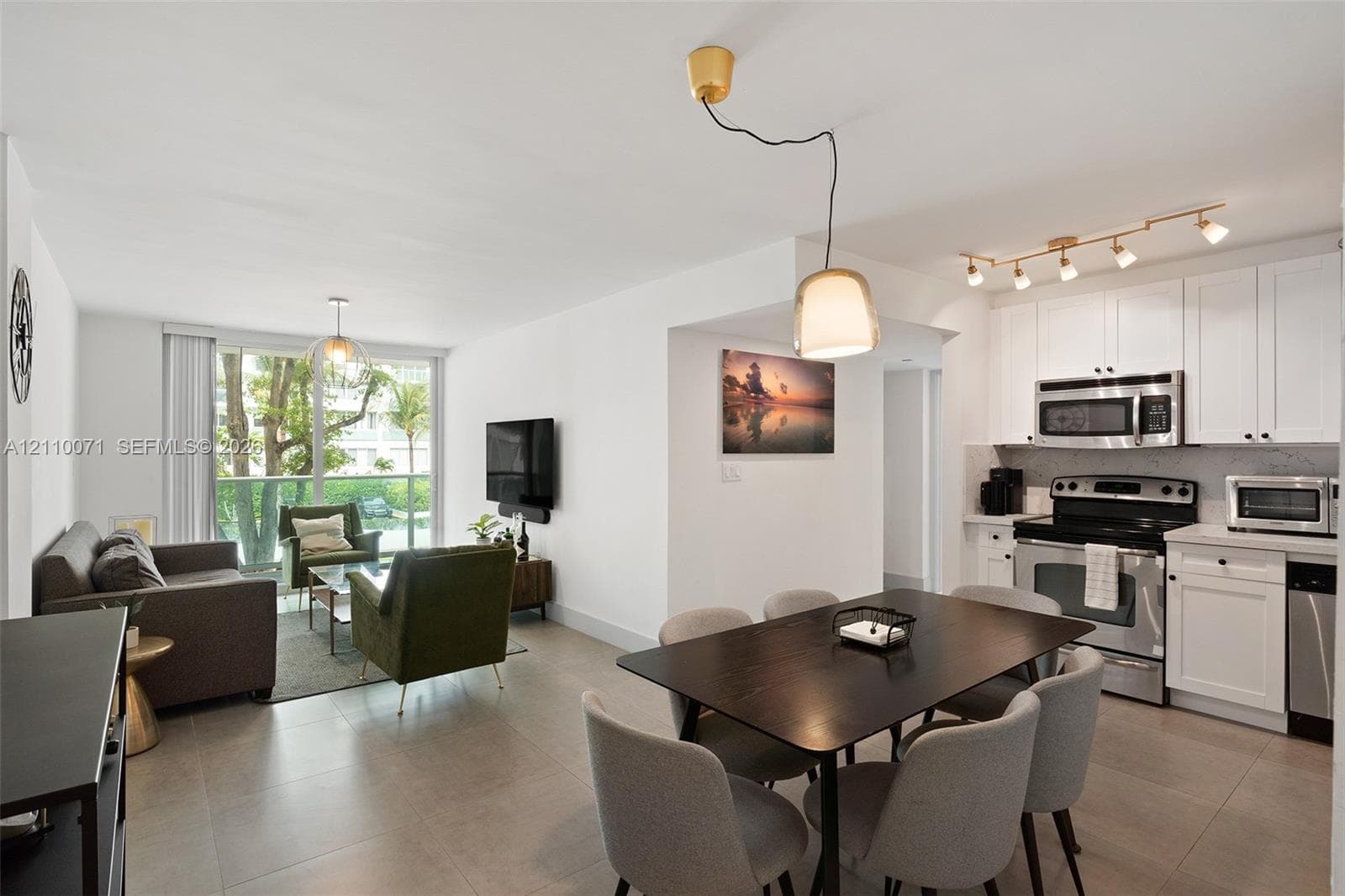 Open-concept interior featuring large-format tile flooring, white cabinetry, stainless steel appliances, and a glass sliding door providing outdoor access