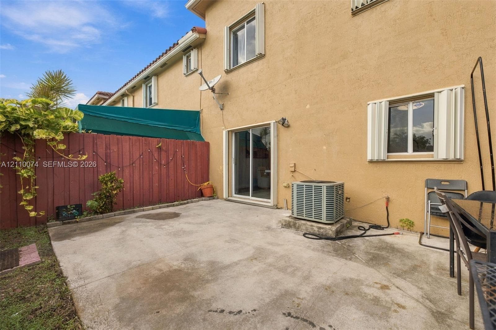 Concrete patio area enclosed by a wood privacy fence featuring sliding glass door access and exterior shutters