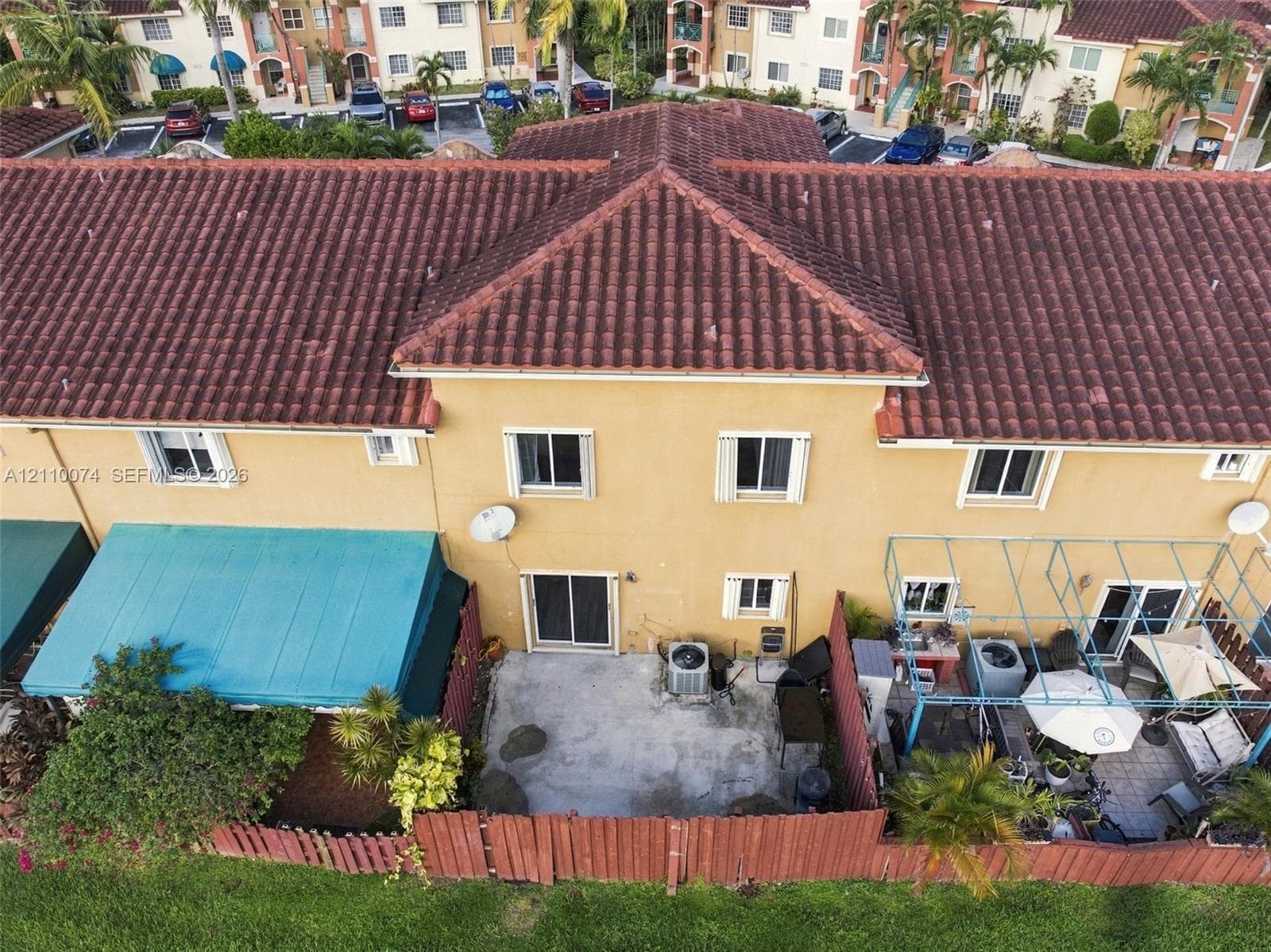 Two-story exterior with clay tile roofing, stucco finish, sliding glass doors, and a private rear patio enclosed by wood fencing