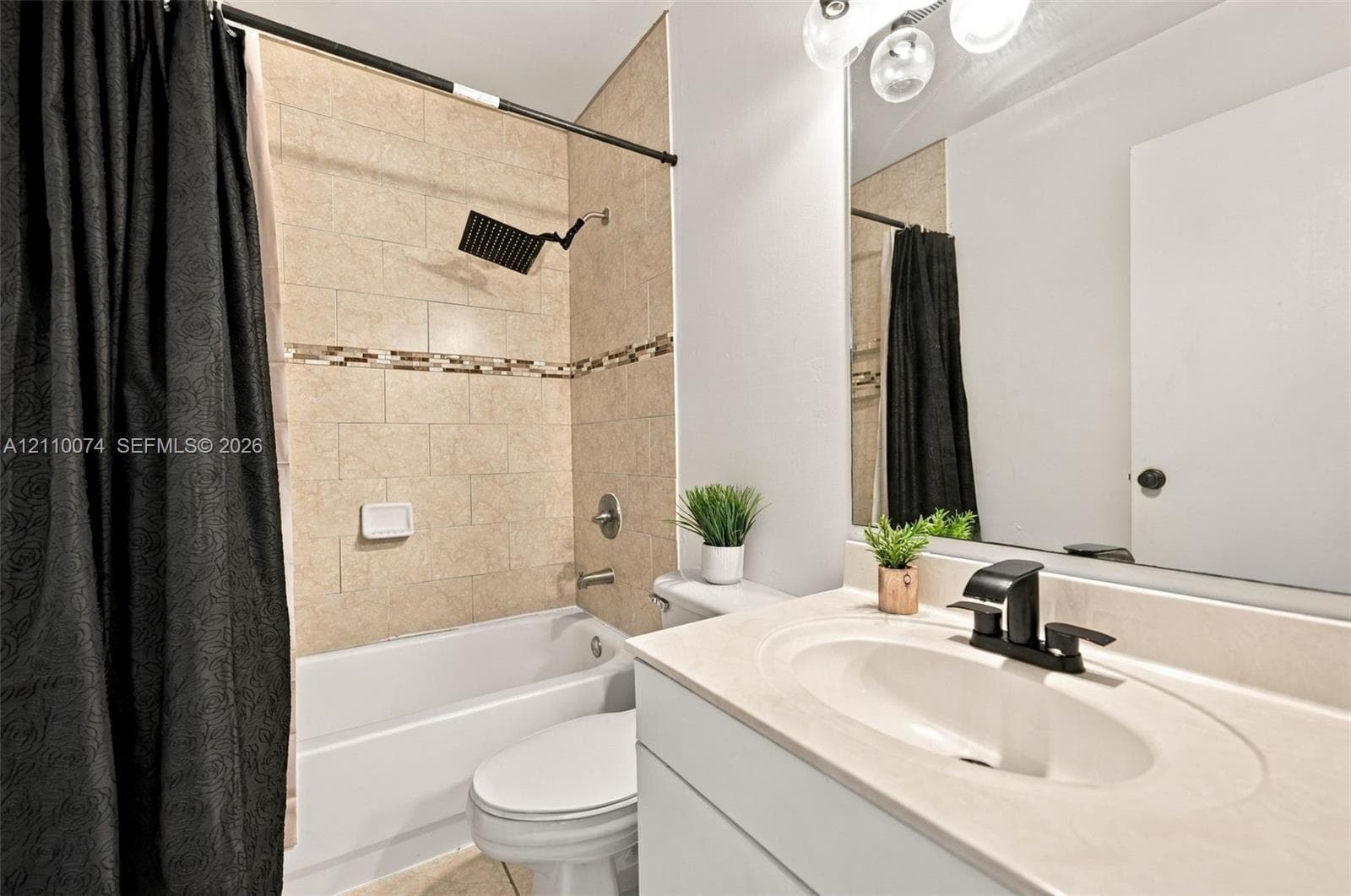 Full bathroom featuring a white vanity with a neutral solid-surface countertop, an integrated oval sink with a matte black faucet, a large wall-mounted mirror, and a bathtub surround tiled in neutral stone-finish ceramic with a decorative glass-tile inlay and a matte black rainfall showerhead