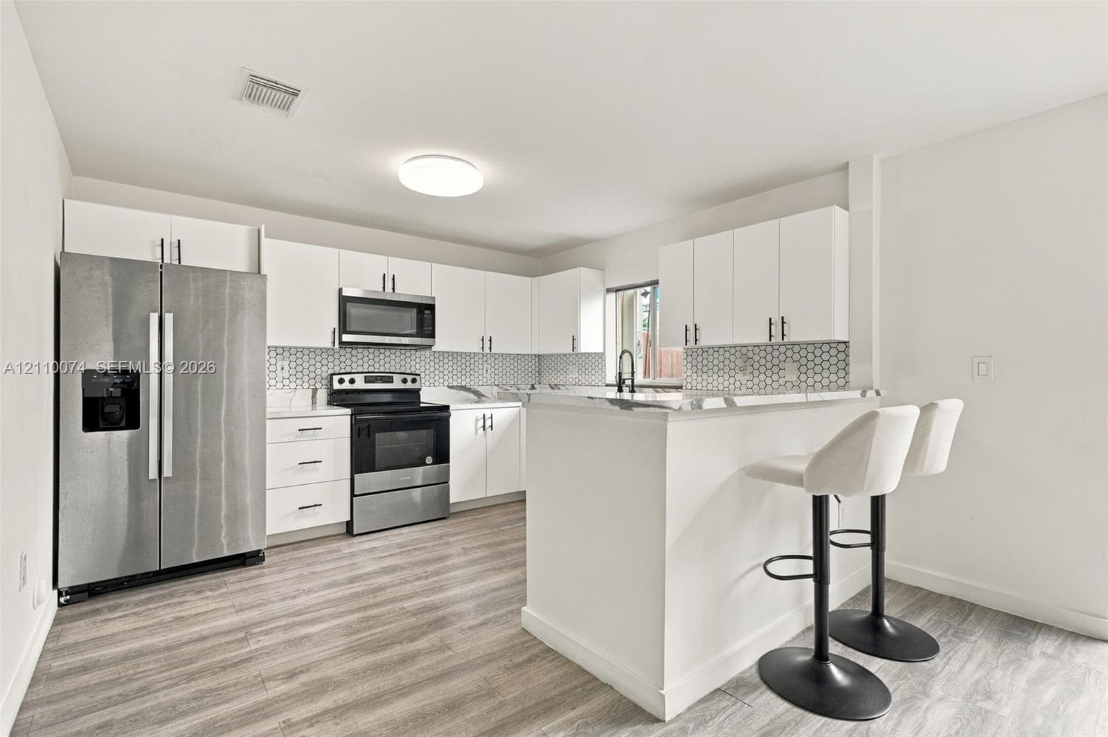 Kitchen featuring white cabinetry, stainless steel appliances, breakfast bar, stone-finish countertops, and wood-finish flooring