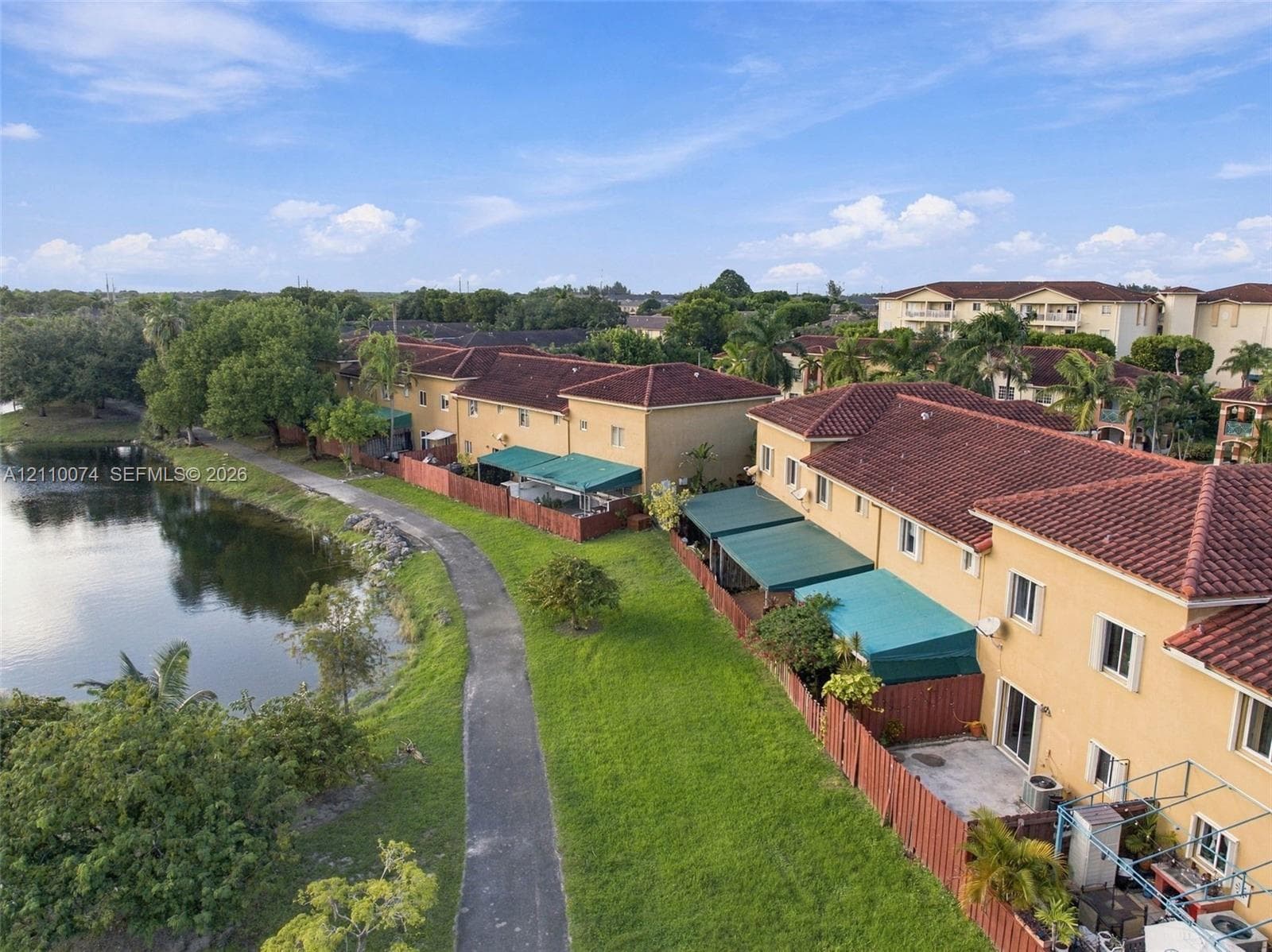 Multi-unit residential complex featuring terracotta-style tile roofing, stucco exterior finish, paved pedestrian pathways, and a water feature