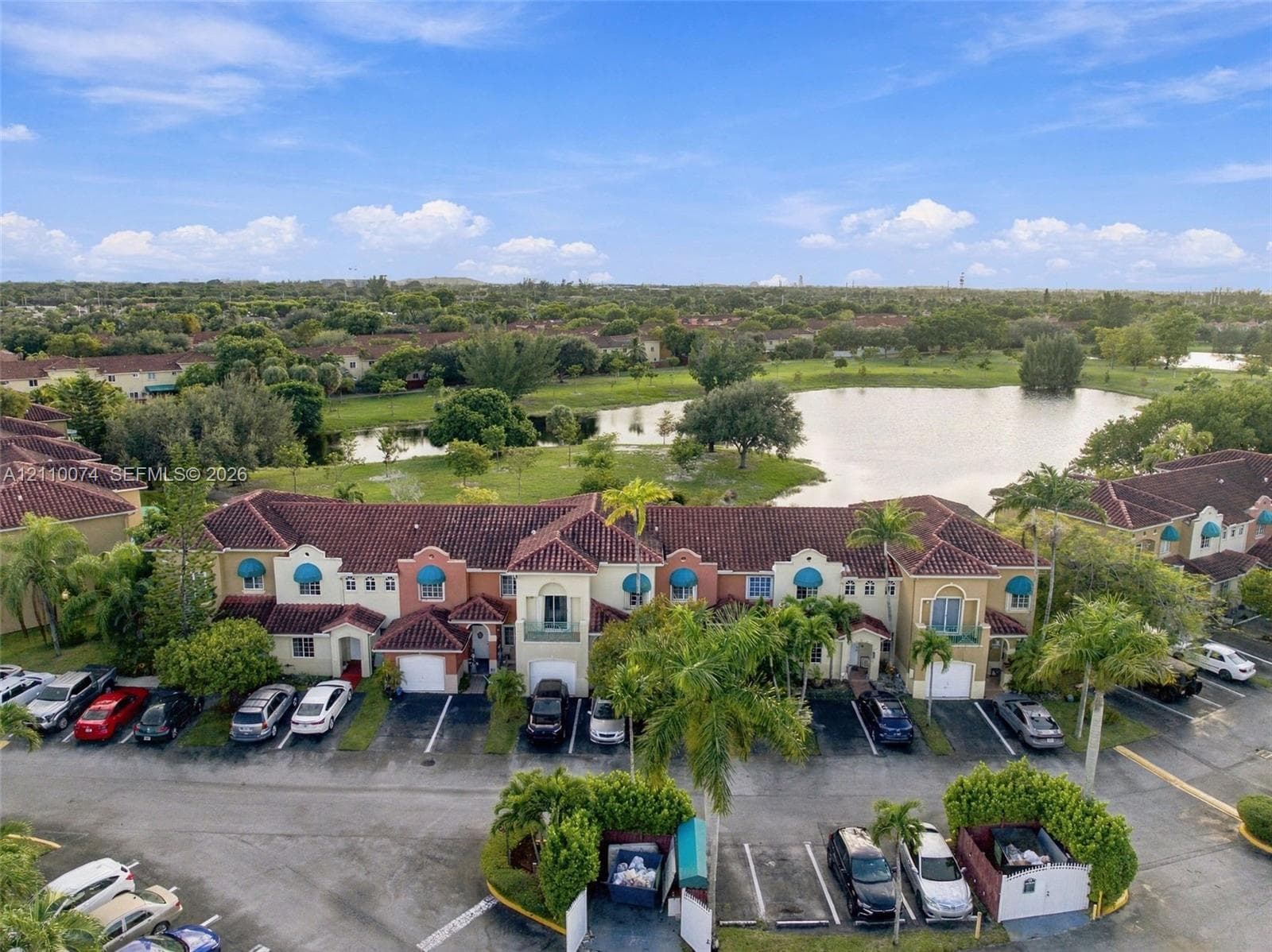 Multi-level townhome exterior featuring terracotta-style roof tiles, stucco facade, decorative blue window awnings, integrated garage bays, and mature palm landscaping